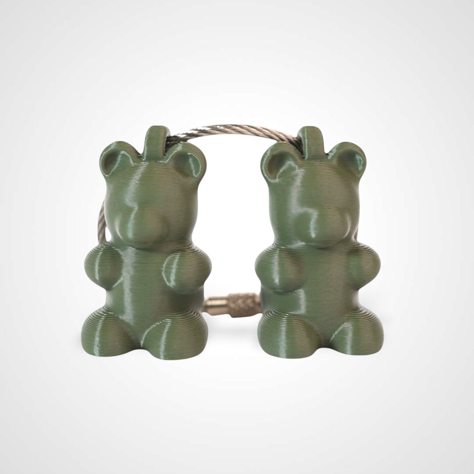 Two army green polylactic acid created using additive manufacturing gummy bear clips on steel cable keyring. Shown on a white background.