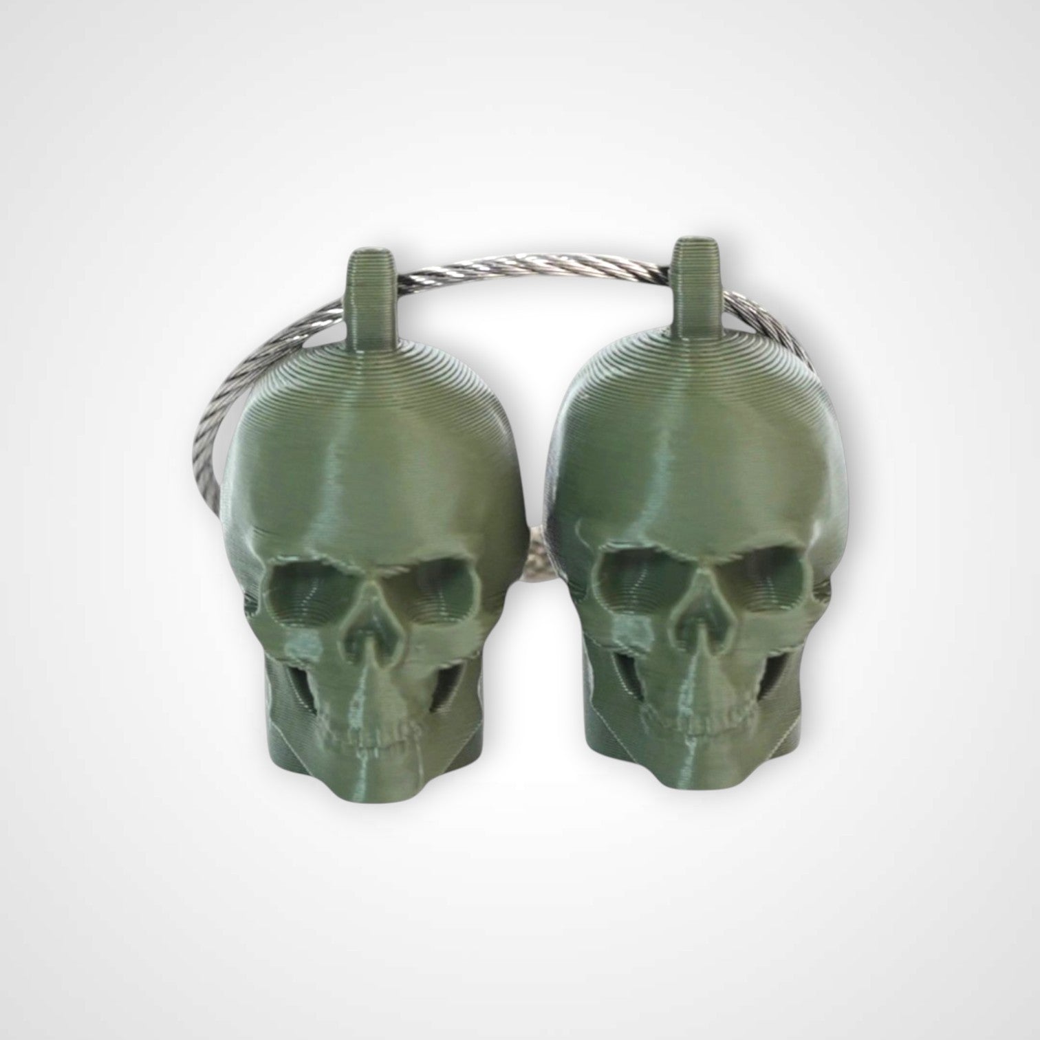 Two army green polylactic acid created using additive manufacturing skull cap clips on steel cable keyring. Shown on a white background.