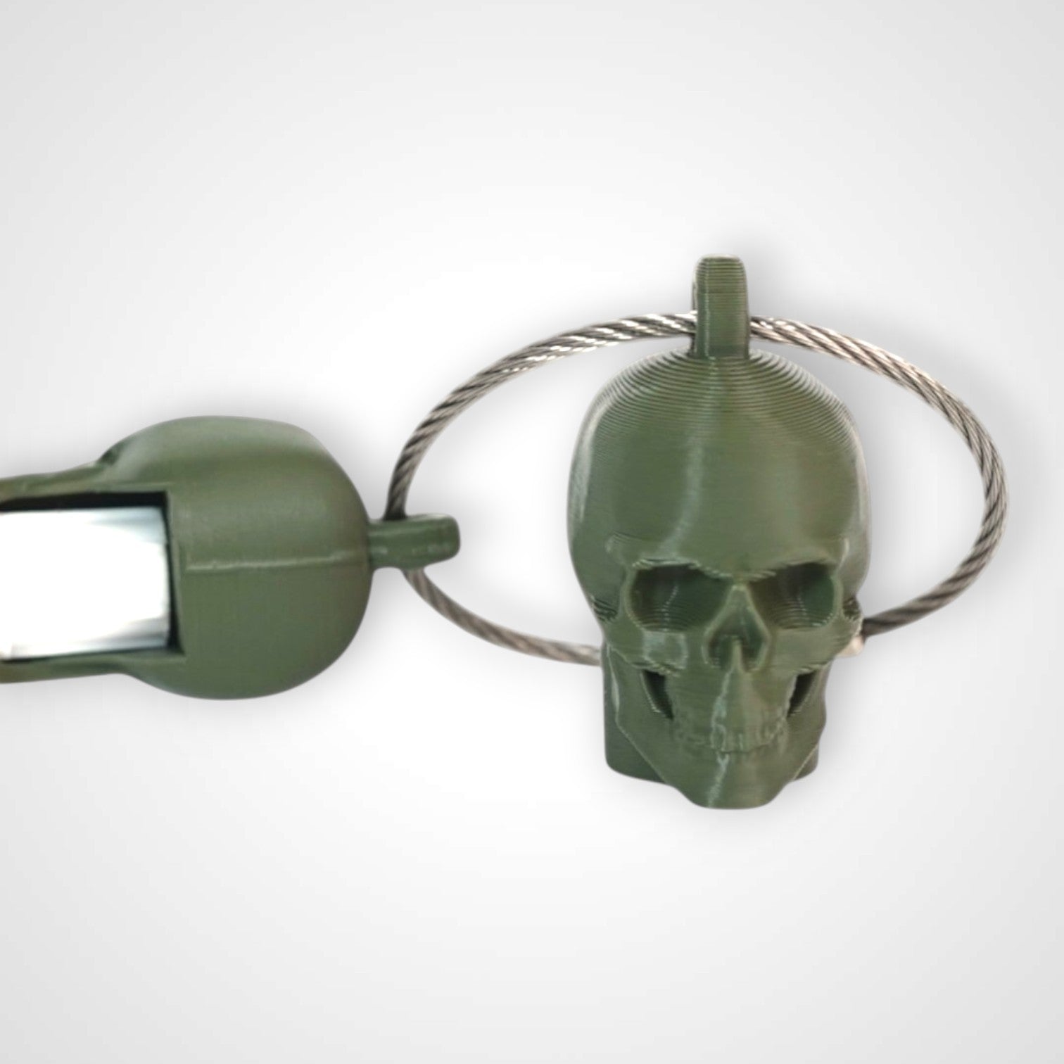 Two army green polylactic acid created using additive manufacturing skull cap clips on steel cable keyring. Featured attached to a syringe. Shown on a white background.