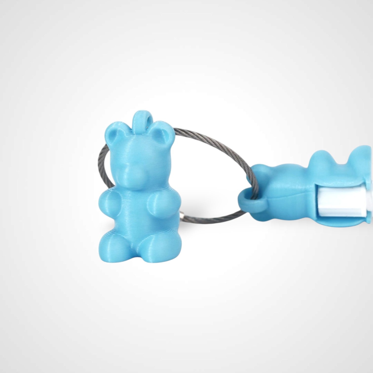 Two teal polylactic acid created using additive manufacturing gummy bear clips on steel cable keyring. Featured attached to a syringe. Shown on a white background.