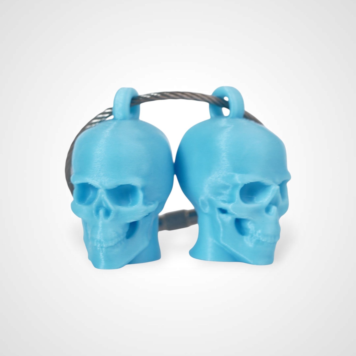 Two blue polylactic acid created using additive manufacturing skull cap clips on steel cable keyring. Shown on a white background.