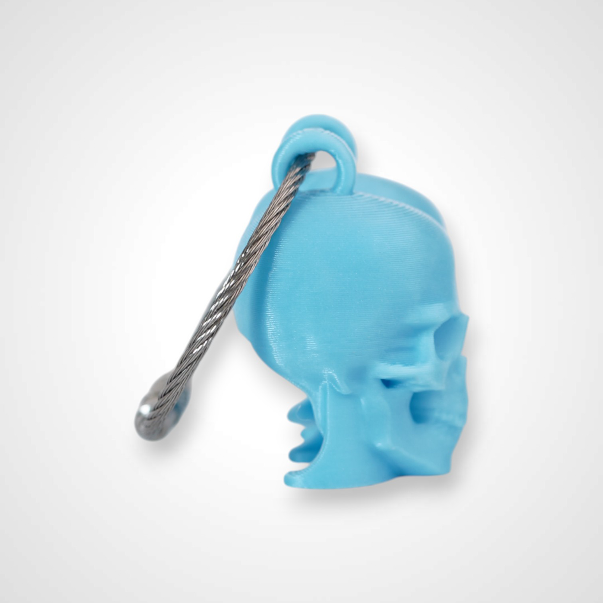 Two blue polylactic acid created using additive manufacturing skull cap clips on steel cable keyring. Shown on a white background.