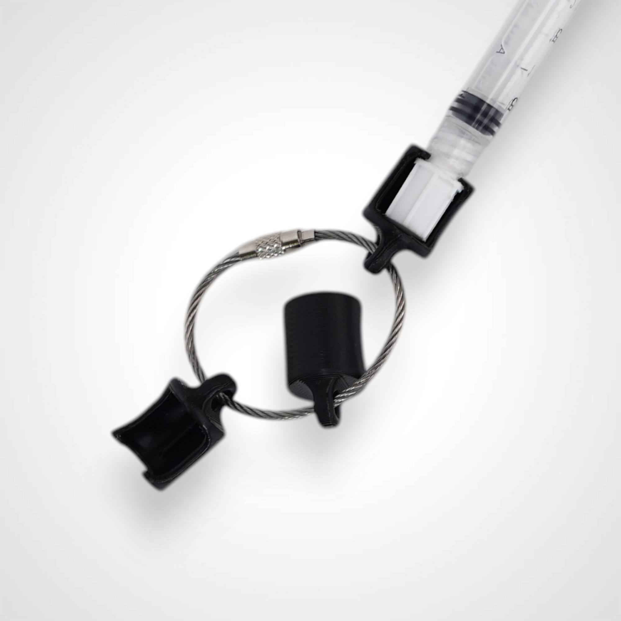 Three black polylactic acid created using additive manufacturing classic cap clips on steel cable keyring. Featured attached to a syringe. Shown on a white background.