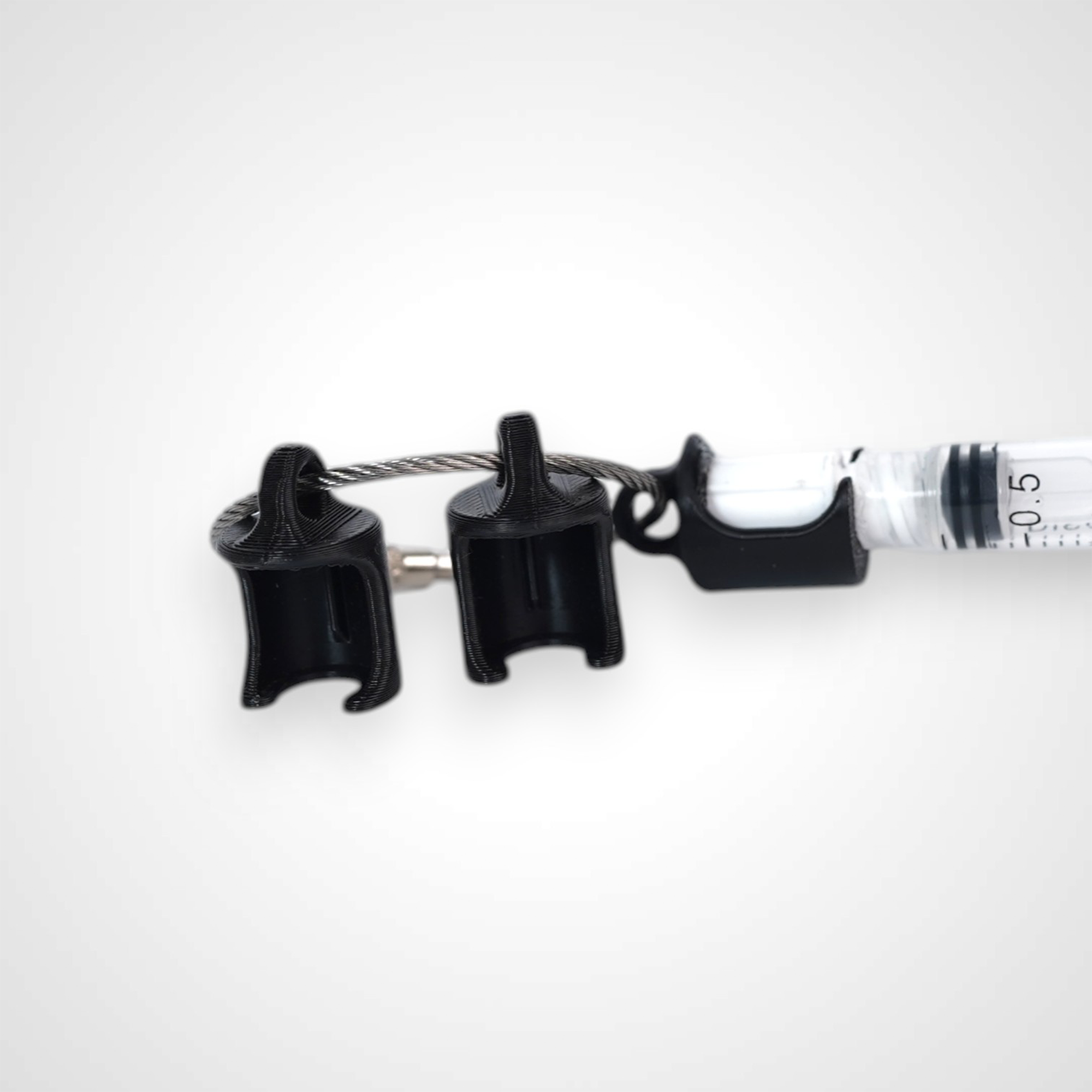 Three black polylactic acid created using additive manufacturing classic cap clips on steel cable keyring. Featured attached to a syringe. Shown on a white background.