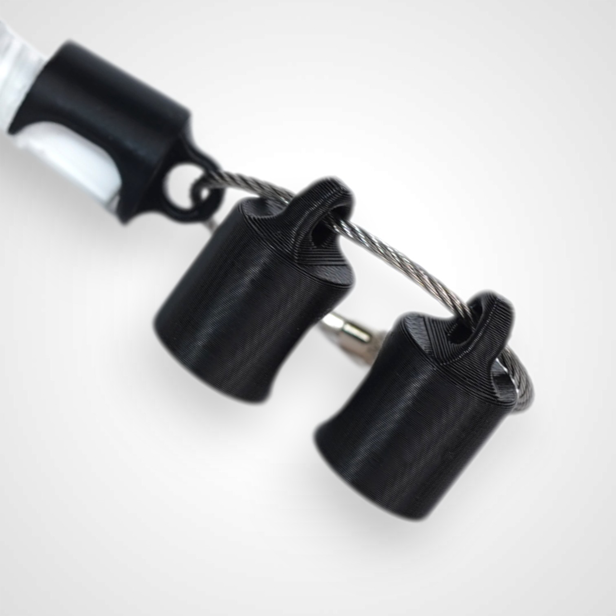 Three black polylactic acid created using additive manufacturing classic cap clips on steel cable keyring. Shown on a white background.