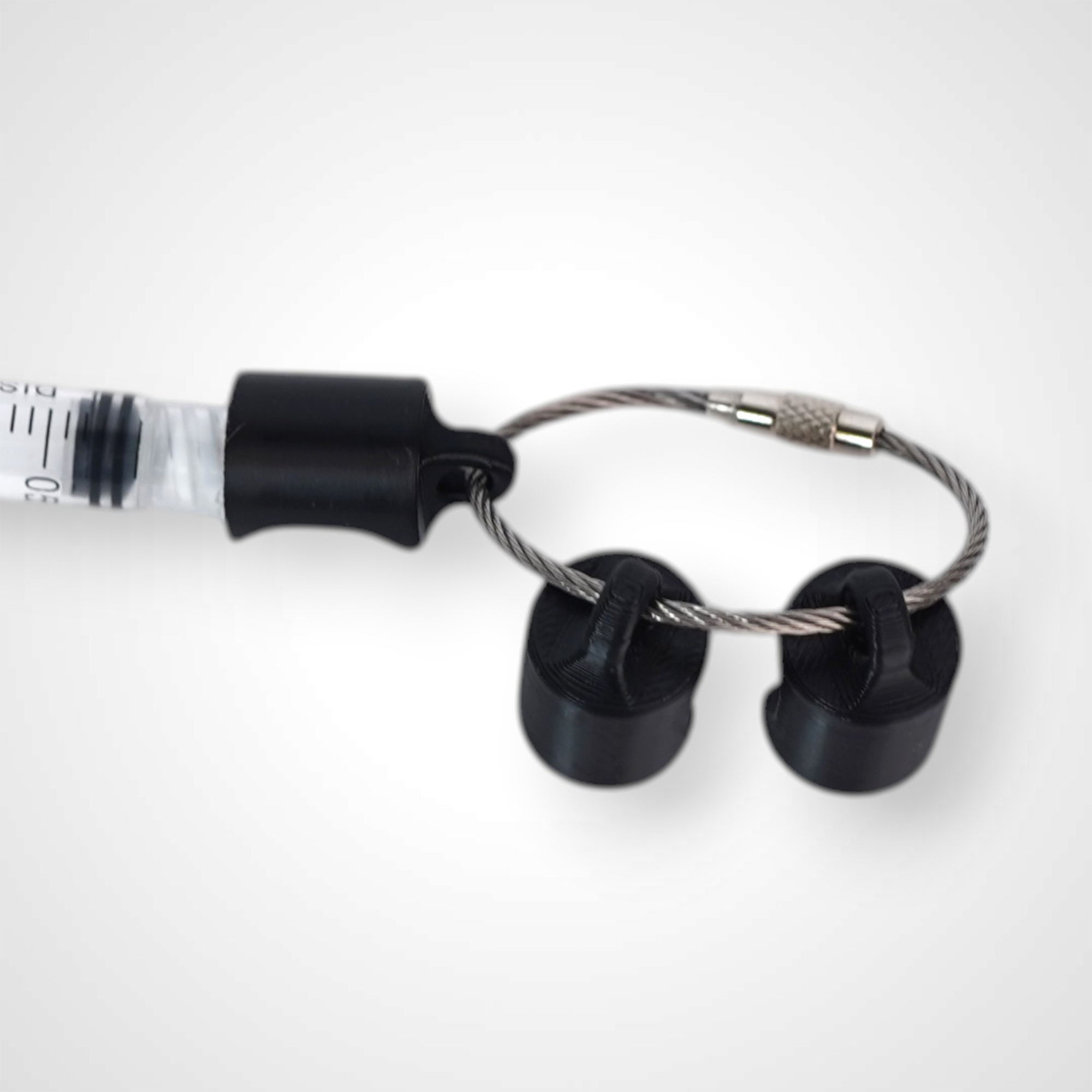 Three black polylactic acid created using additive manufacturing classic cap clips on steel cable keyring. Featured attached to a syringe. Shown on a white background.
