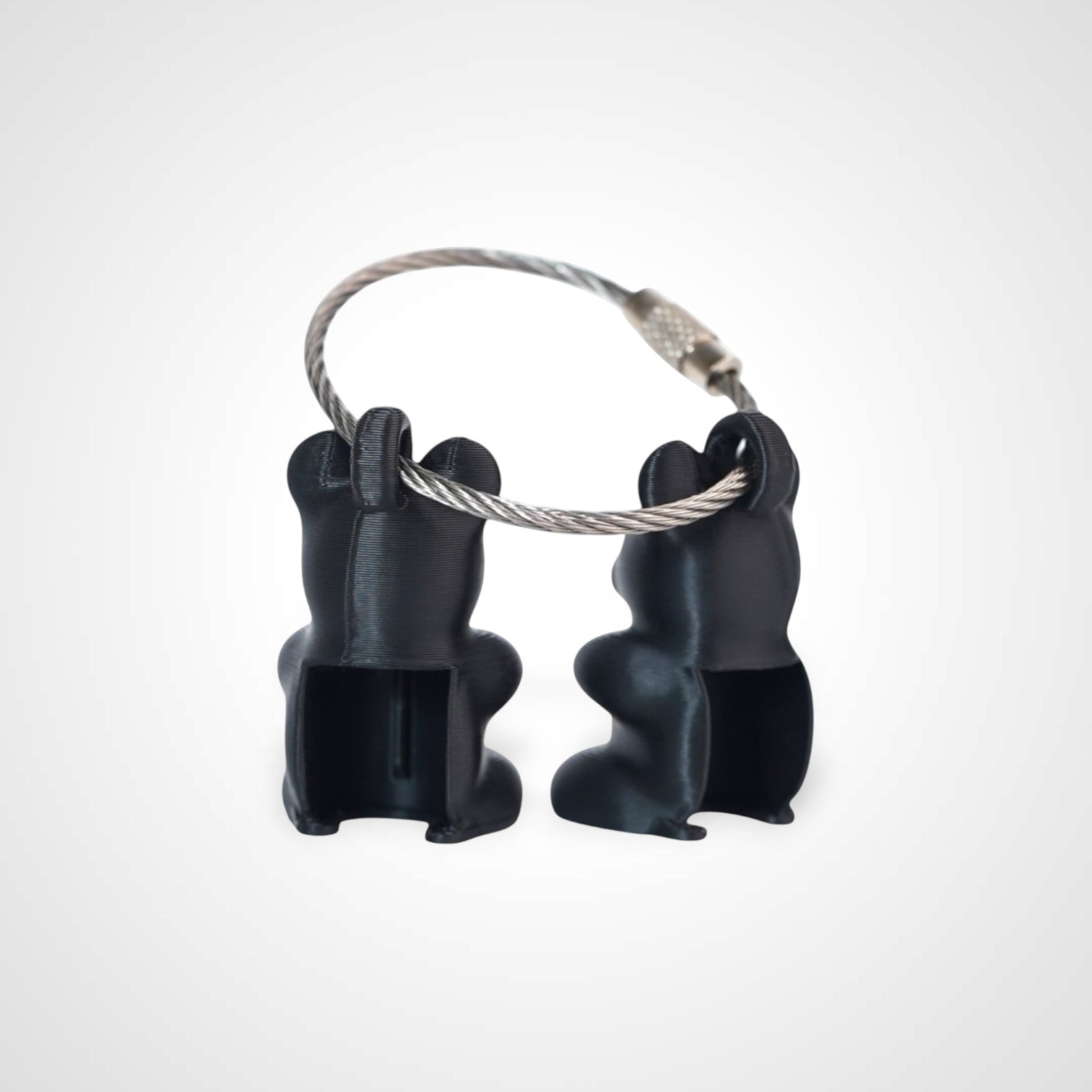 Two black polylactic acid created using additive manufacturing gummy bear cap clips on steel cable keyring. Shown on a white background.