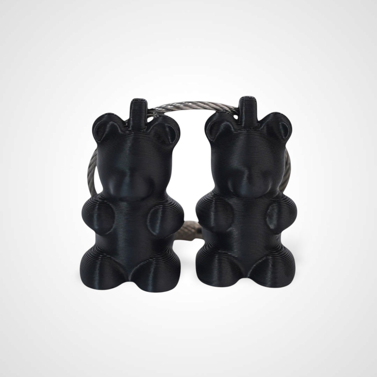 Two black polylactic acid created using additive manufacturing gummy bear cap clips on steel cable keyring. Shown on a white background.