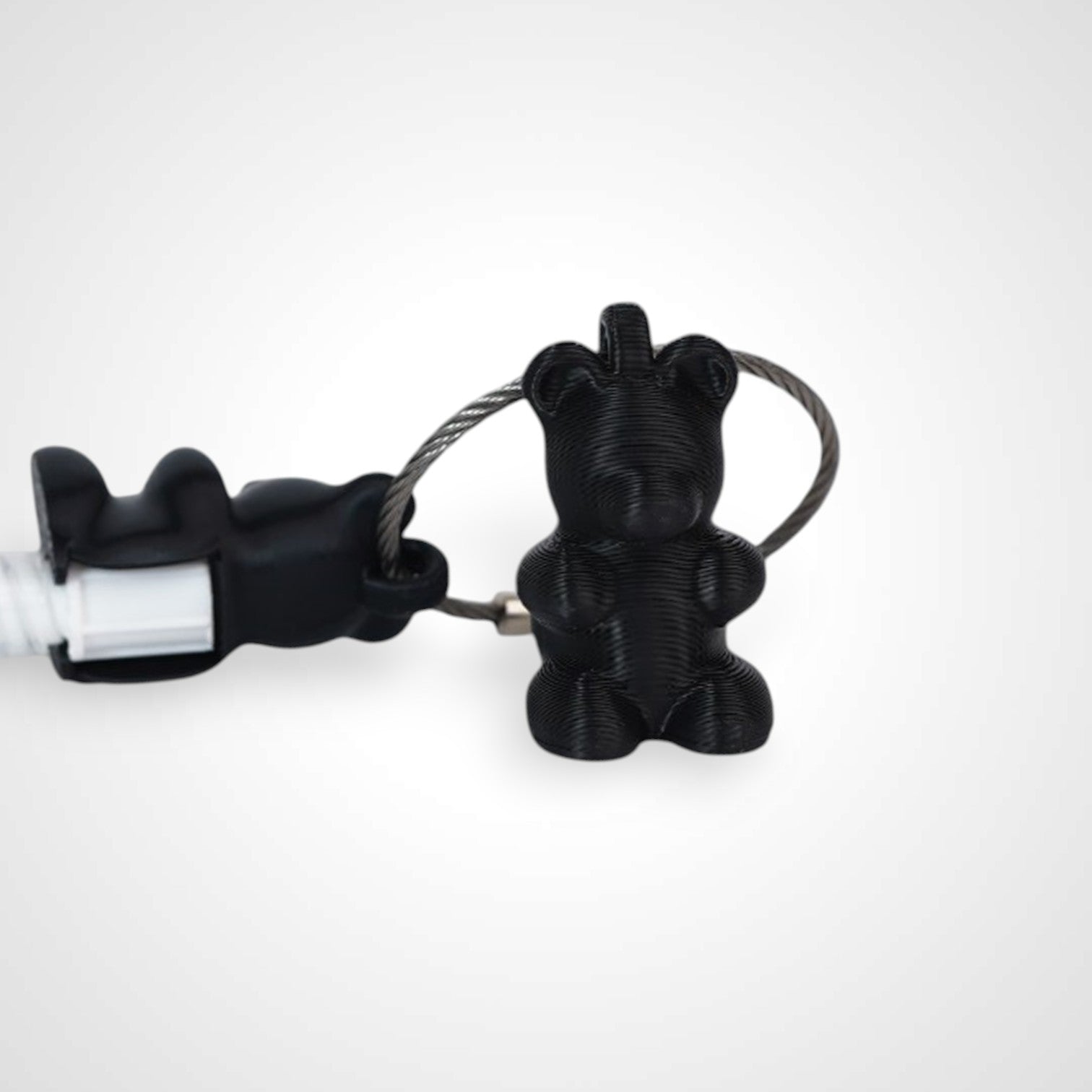 Two black polylactic acid created using additive manufacturing gummy bear cap clips on steel cable keyring. Featured attached to a syringe. Shown on a white background.