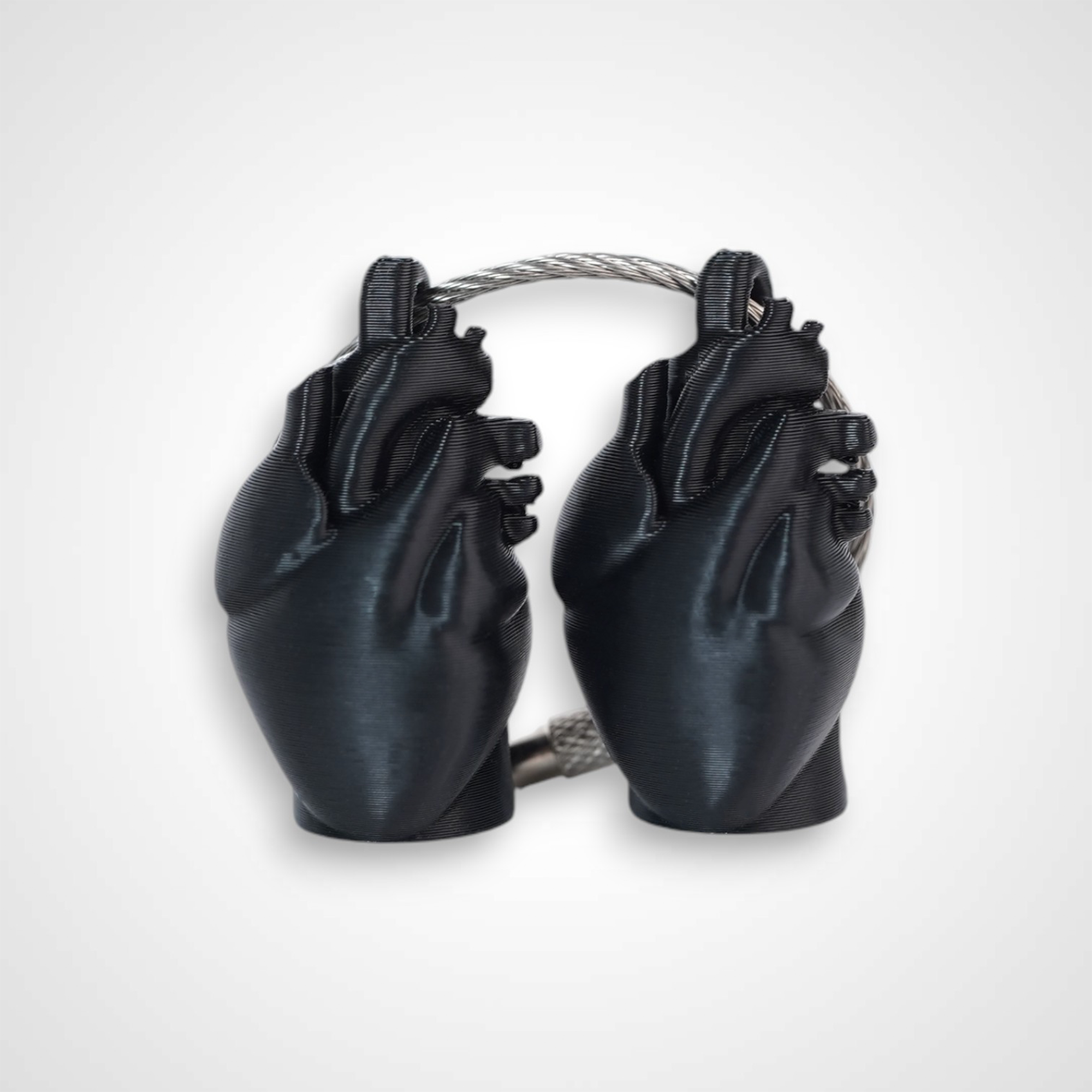 Two black polylactic acid created using additive manufacturing anatomical heart cap clips on steel cable keyring. Shown on a white background.