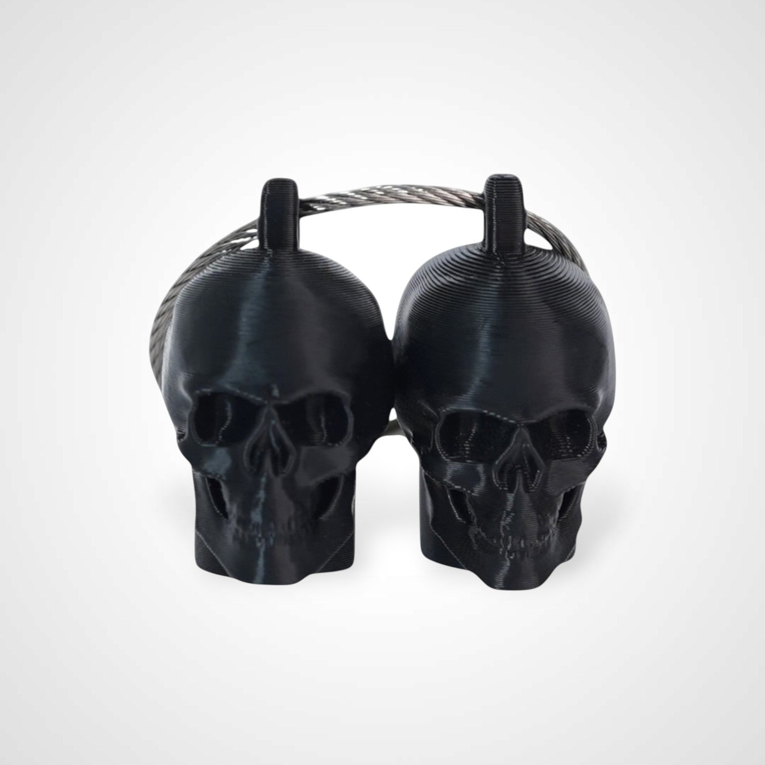 Two black polylactic acid created using additive manufacturing skull cap clips on steel cable keyring. Shown on a white background.