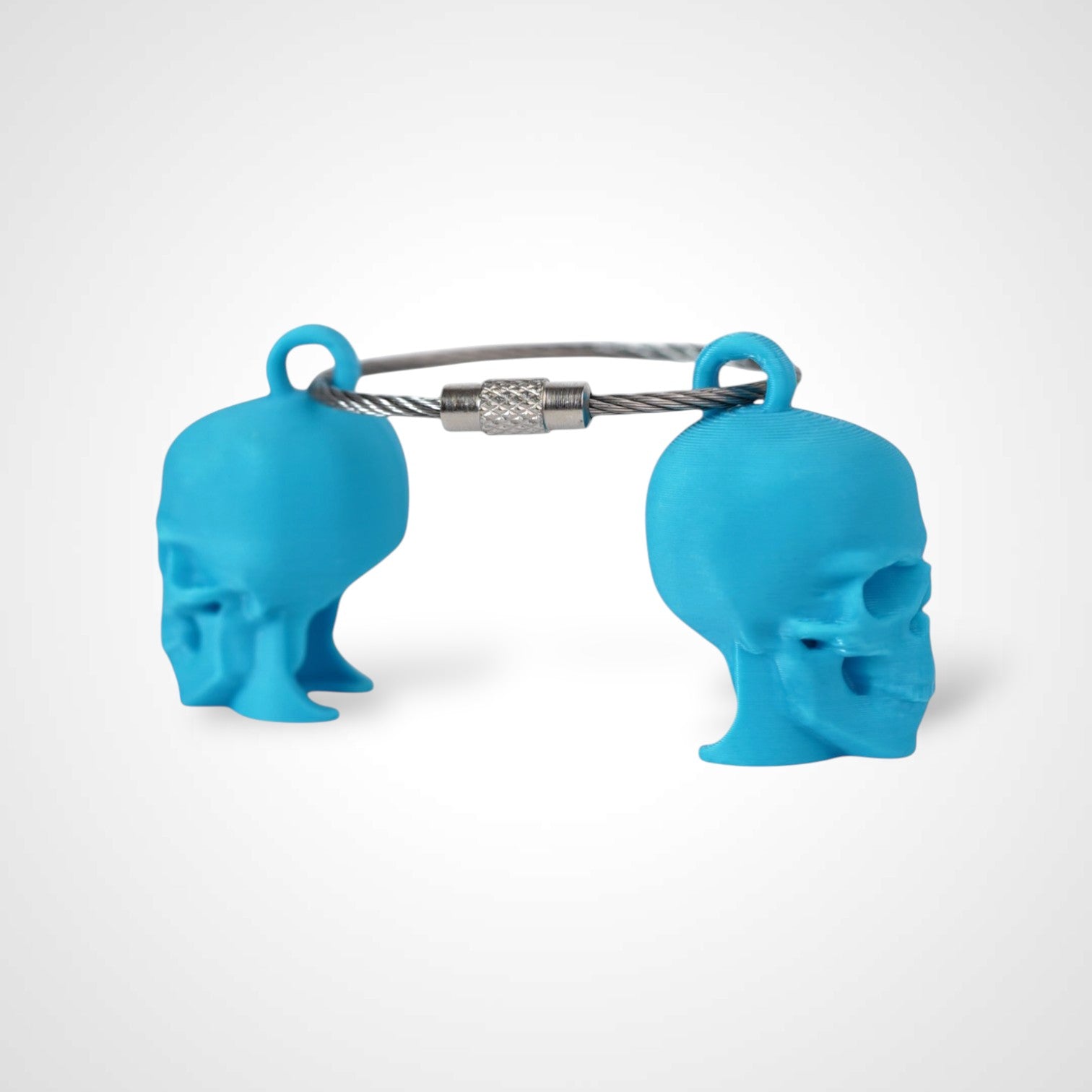 Two blue polylactic acid created using additive manufacturing skull cap clips on steel cable keyring. Shown on a white background.