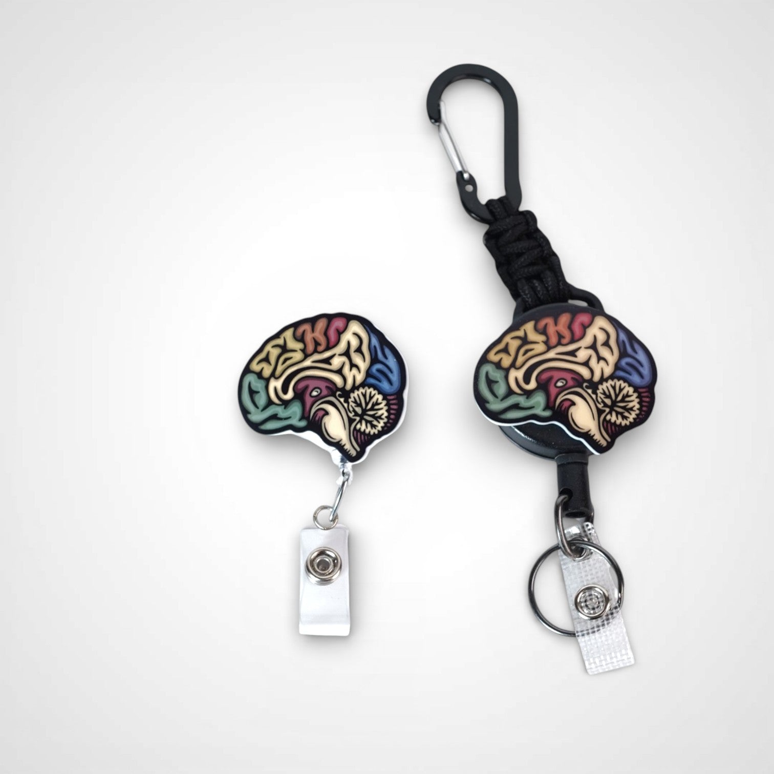 Sagittal brain badge reel. On a carabiner with a steel retractable cable next to a swivel-alligator clip that rotates 360° with a nylon retractable string. Shown on a white background.