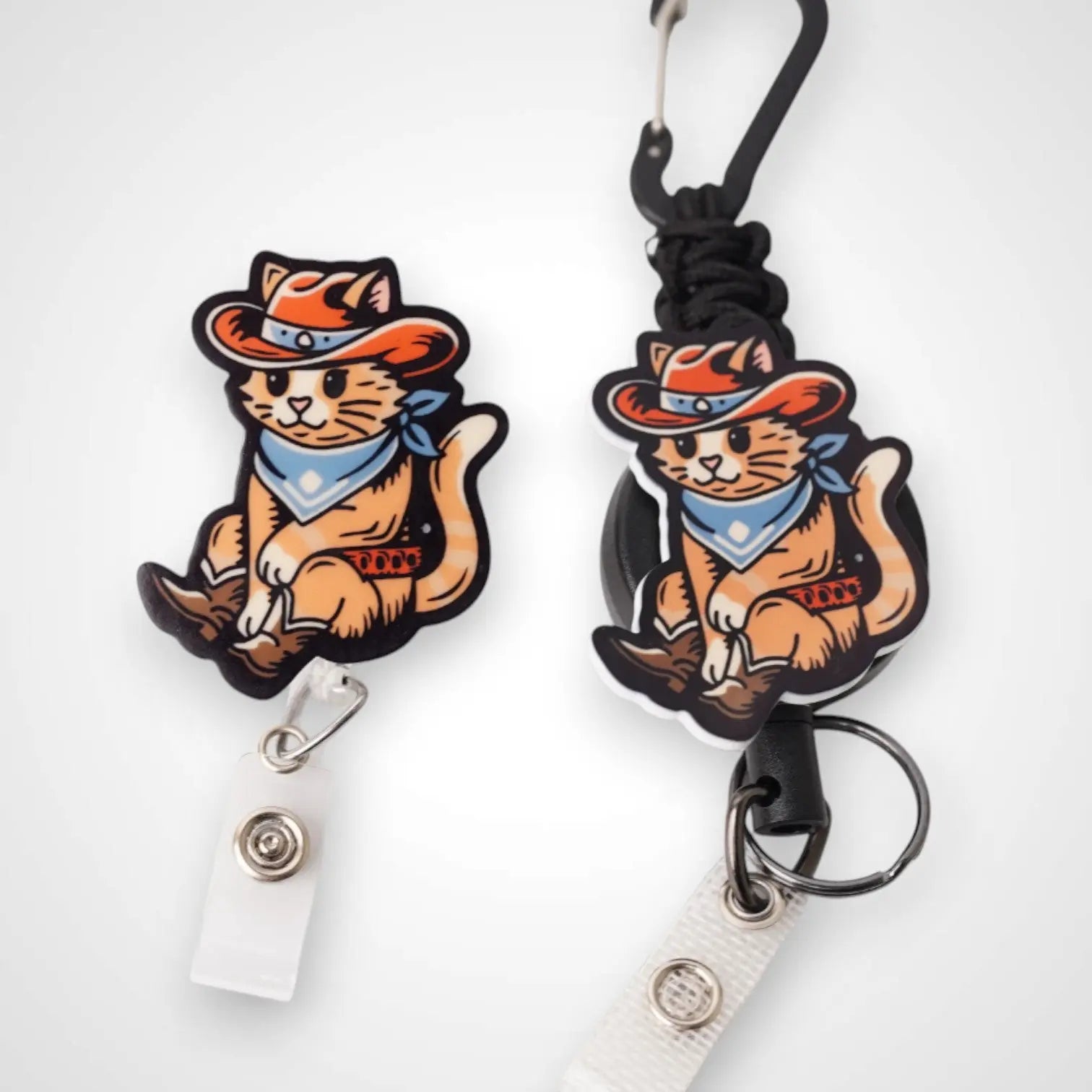 Cowboy Cat badge reel. On a carabiner with a steel retractable cable next to a swivel-alligator clip that rotates 360° with a nylon retractable string. Shown on a white background.