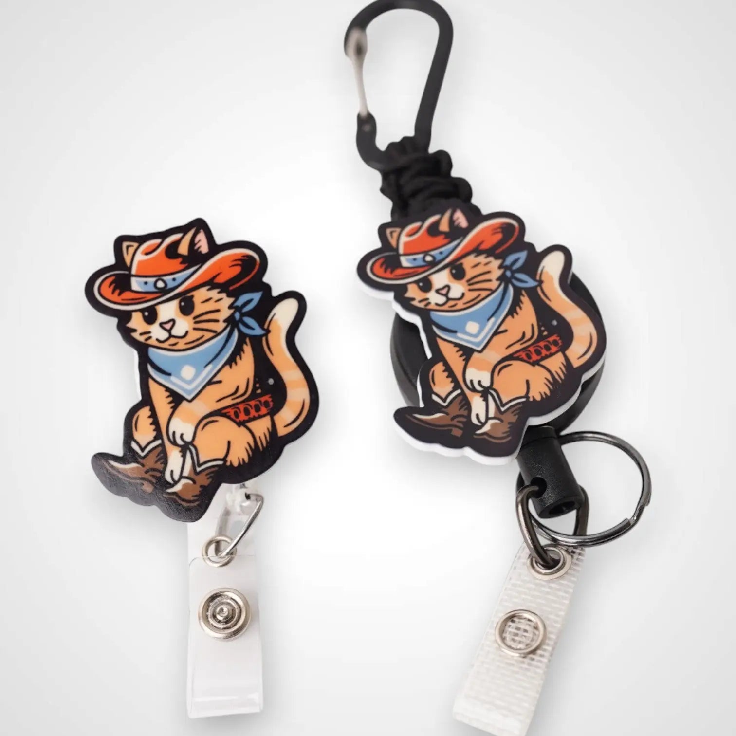 Cowboy Cat badge reel. On a carabiner with a steel retractable cable next to a swivel-alligator clip that rotates 360° with a nylon retractable string. Shown on a white background.
