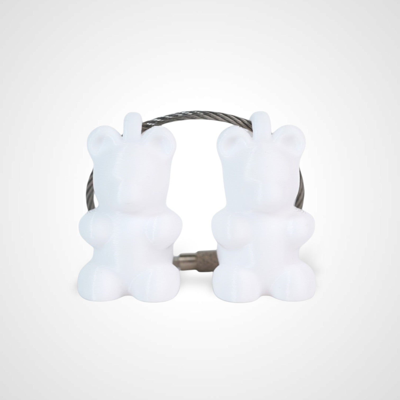 Two white polylactic acid created using additive manufacturing gummy bear cap clips on steel cable keyring. Shown on a white background.