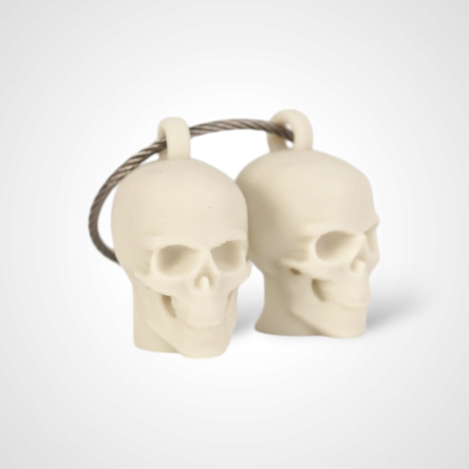 Two off white polylactic acid created using additive manufacturing skull cap clips on steel cable keyring. Shown on a white background.