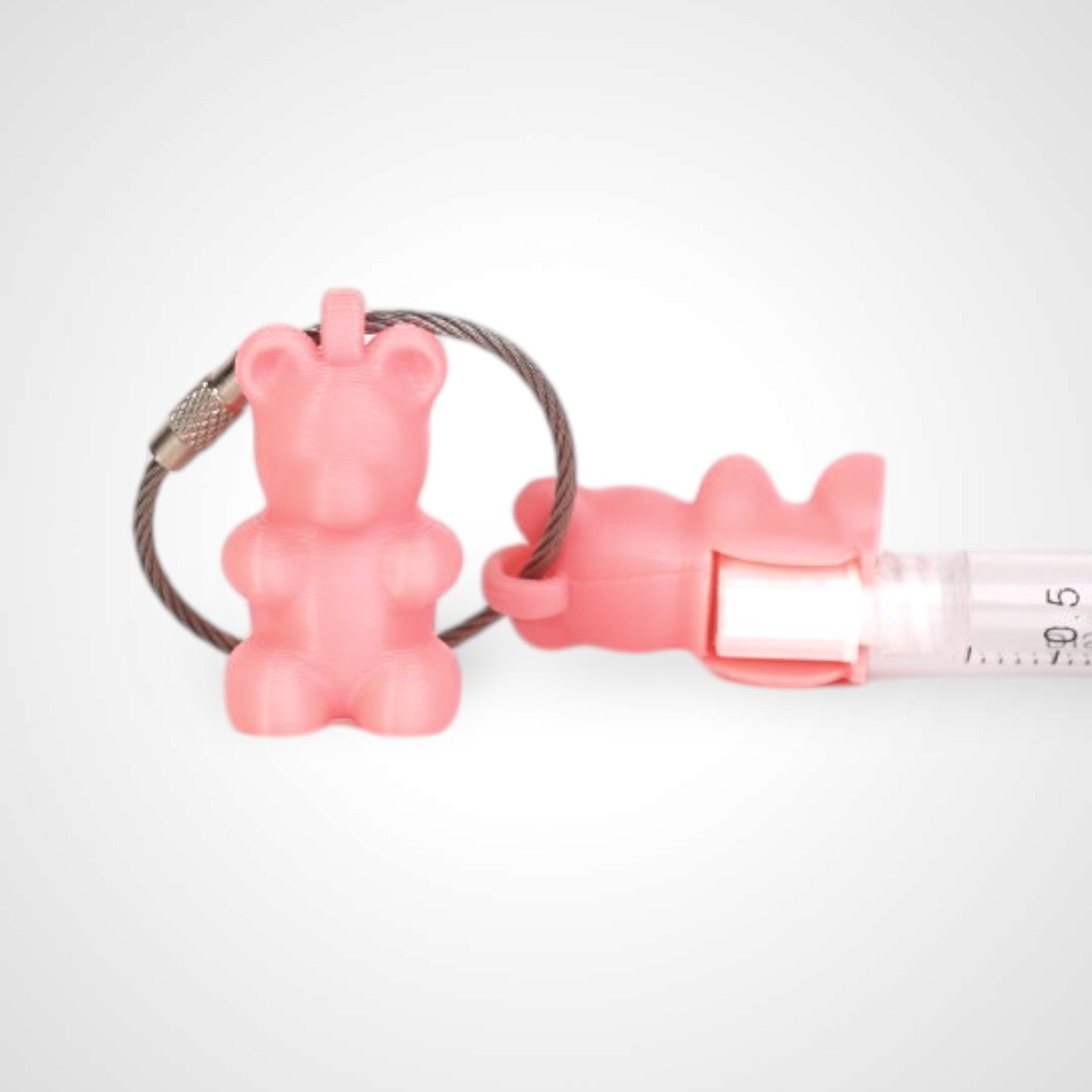 Two pink polylactic acid created using additive manufacturing gummy bear cap clips on steel cable keyring. Featured attached to a syringe. Shown on a white background.