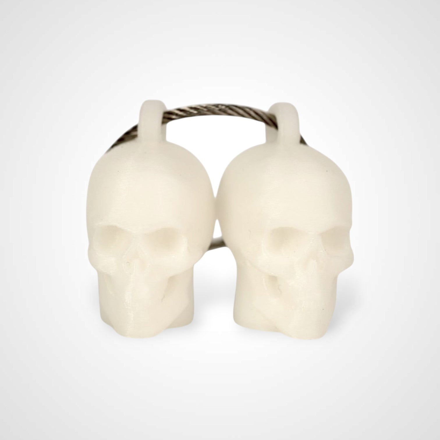 Two white polylactic acid created using additive manufacturing skull cap clips on steel cable keyring. Shown on a white background.