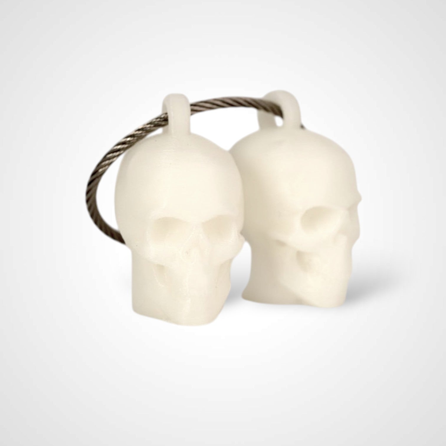 Two white polylactic acid created using additive manufacturing skull cap clips on steel cable keyring. Shown on a white background.