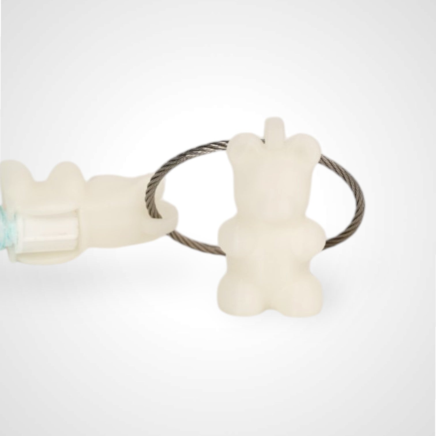 Two white polylactic acid created using additive manufacturing gummy bear cap clips on steel cable keyring. Featured attached to a syringe. Shown on a white background.