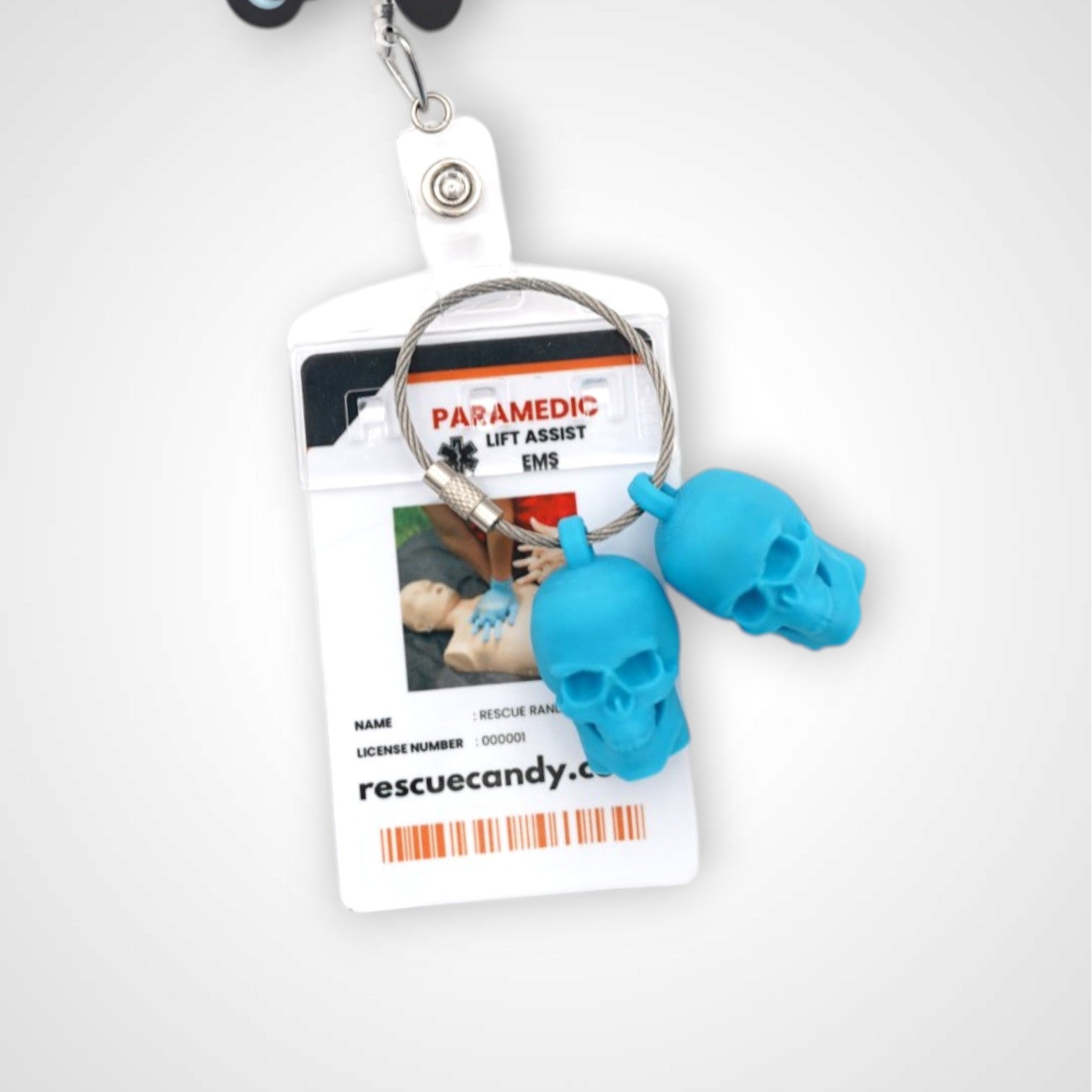 Two blue polylactic acid created using additive manufacturing skull cap clips on steel cable keyring. Featured attached to a badge. Shown on a white background.