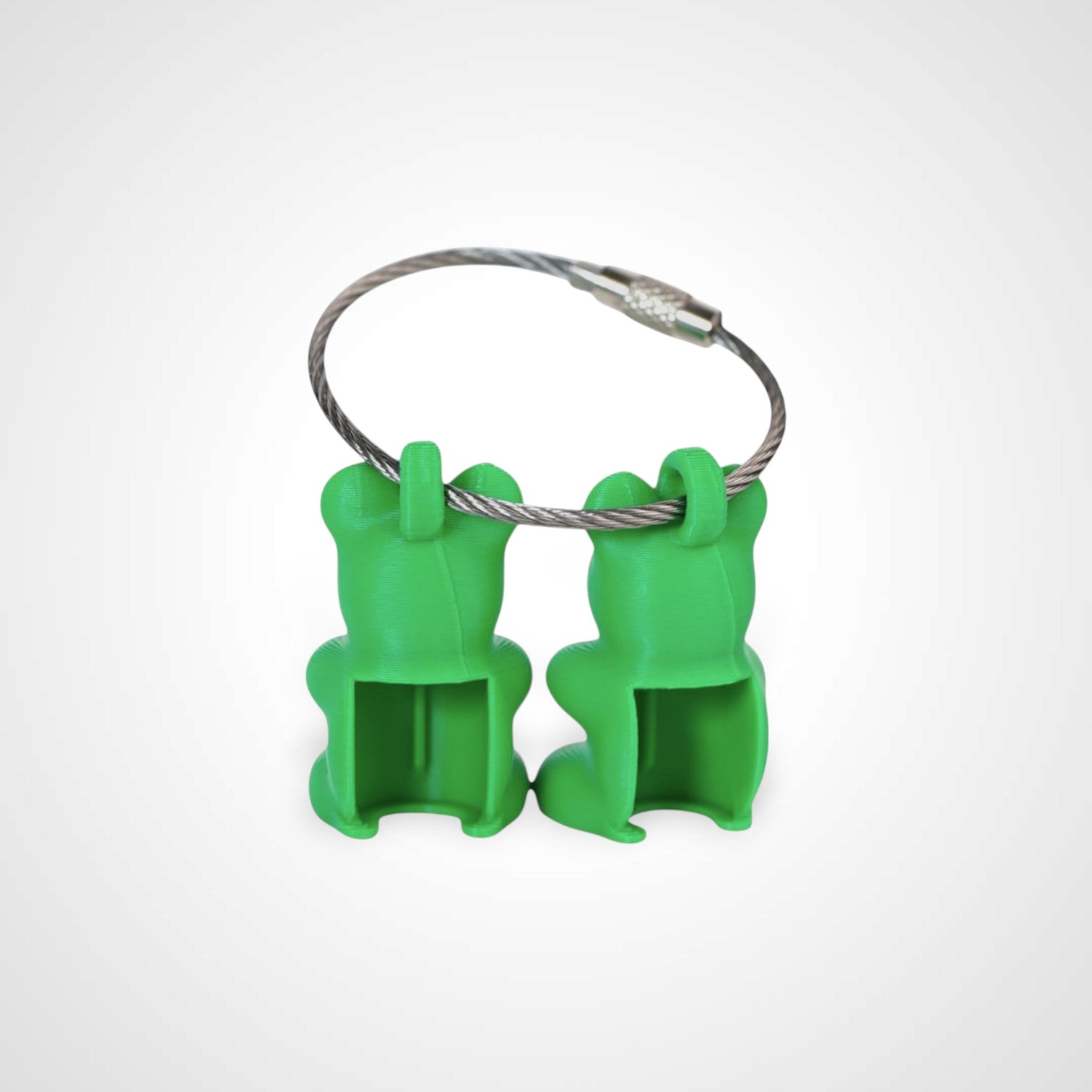 Two green polylactic acid created using additive manufacturing gummy bear cap clips on steel cable keyring. Shown on a white background.
