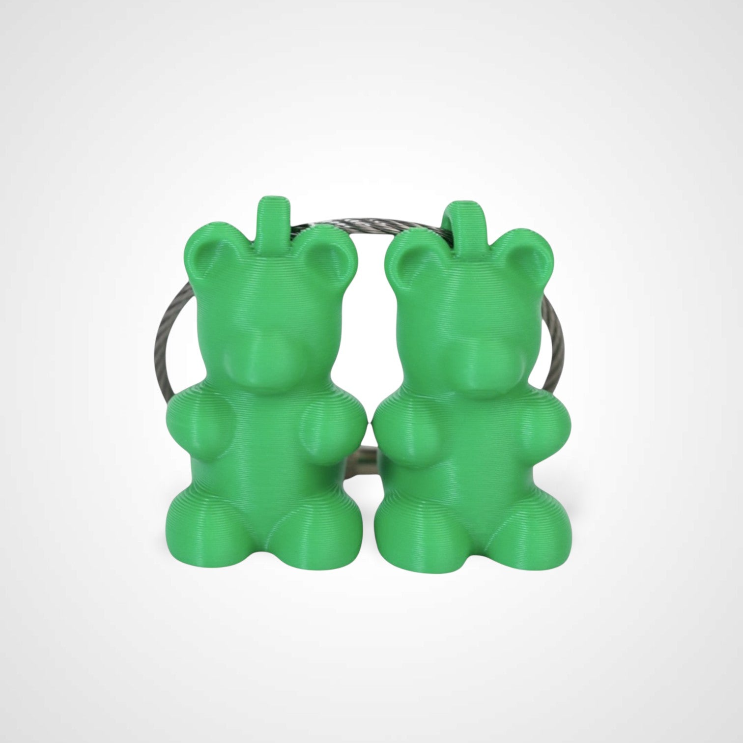 Two green polylactic acid created using additive manufacturing gummy bear cap clips on steel cable keyring. Shown on a white background.