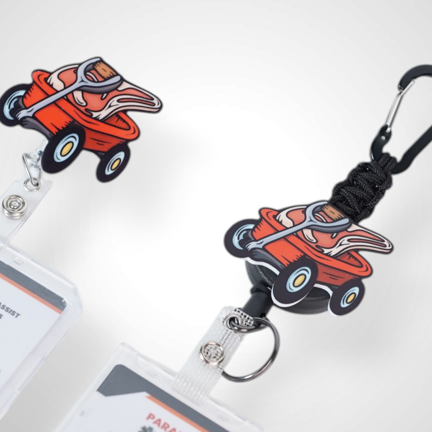 Meat wagon badge reel. On a carabiner with a steel retractable cable next to a swivel-alligator clip that rotates 360° with a nylon retractable string. Shown on a white background.