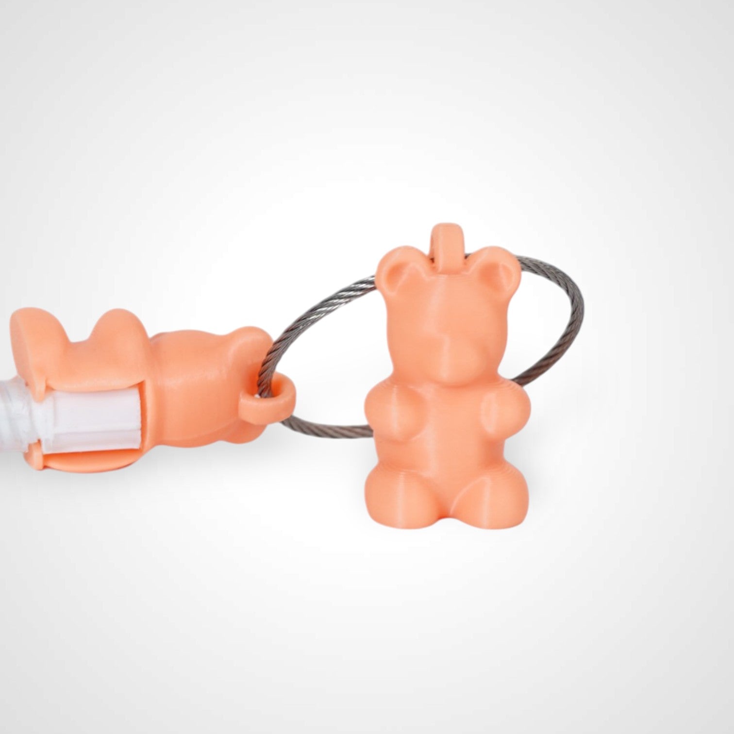 Two orange polylactic acid created using additive manufacturing gummy bear clips on steel cable keyring. Featured attached to a syringe. Shown on a white background.
