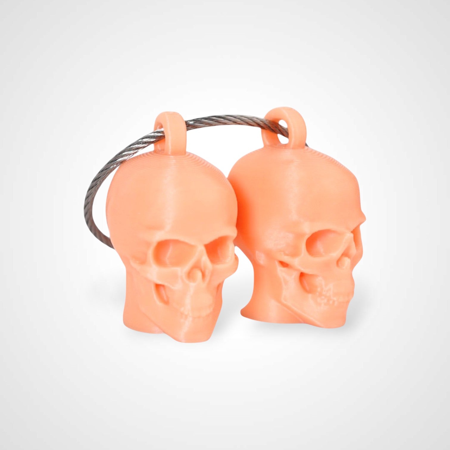 Two orange polylactic acid created using additive manufacturing skull cap clips on steel cable keyring. Shown on a white background.