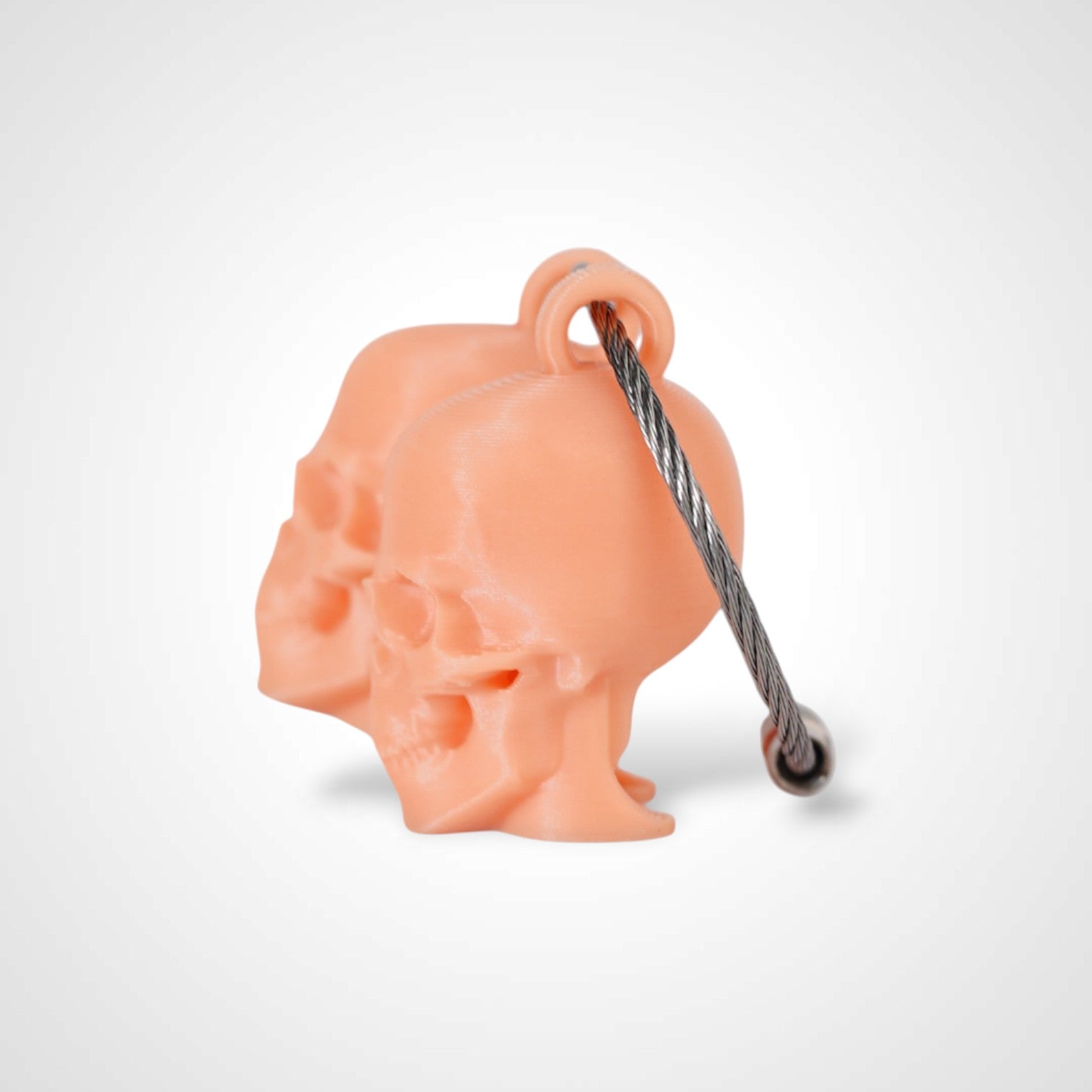 Two orange polylactic acid created using additive manufacturing skull cap clips on steel cable keyring. Shown on a white background.