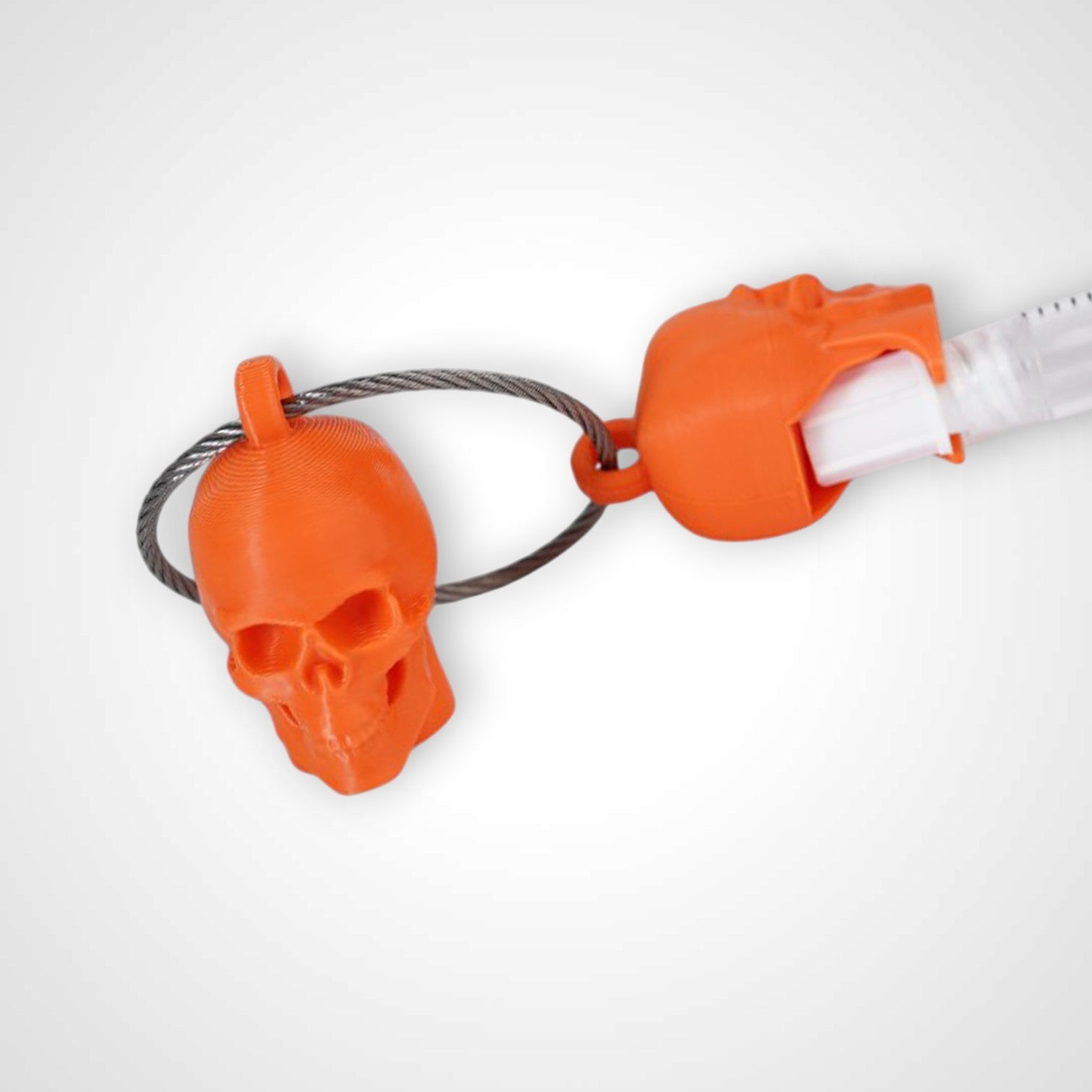 Two orange polylactic acid created using additive manufacturing skull cap clips on steel cable keyring. Featured attached to a syringe. Shown on a white background.