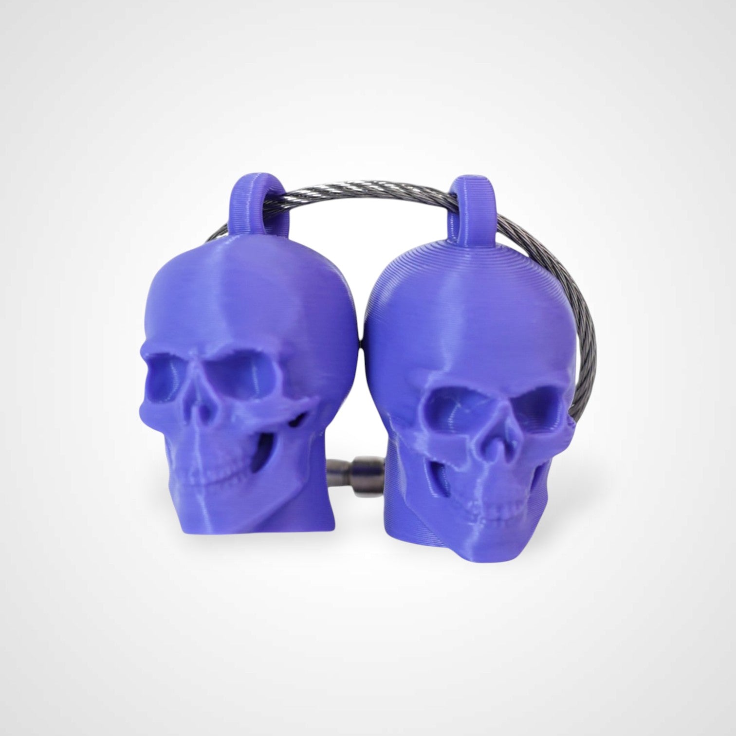 Two purple polylactic acid created using additive manufacturing skull cap clips on steel cable keyring. Shown on a white background.