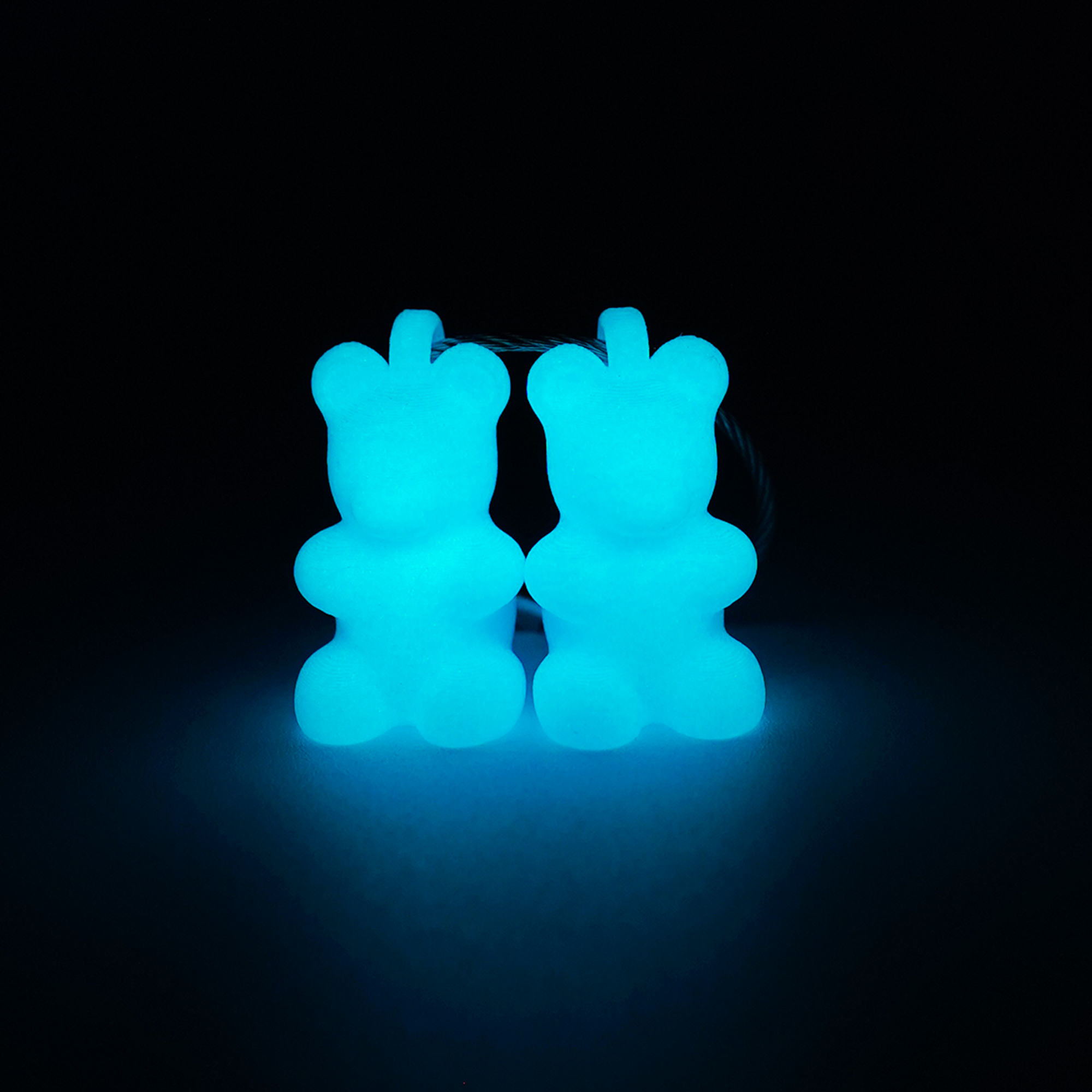 Two teal polylactic acid created using additive manufacturing gummy bear clips on steel cable keyring. Shown glowing blue on a black background.
