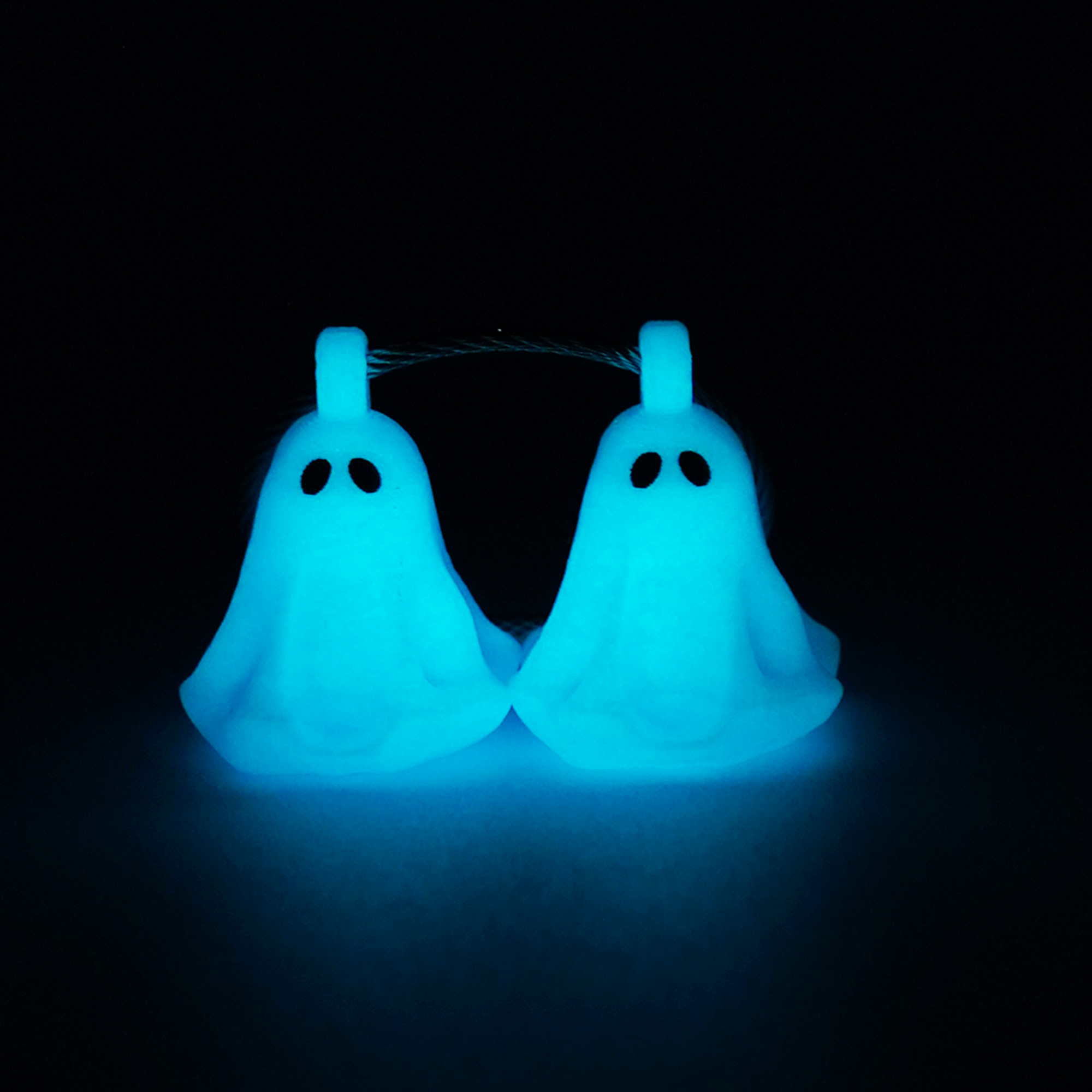 Two blue polylactic acid created using additive manufacturing ghost cap clips on steel cable keyring. Shown glowing blue on a black background.