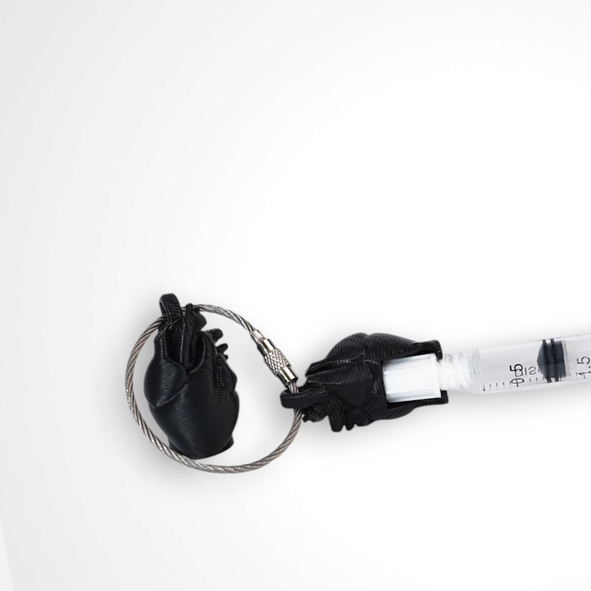 Two black polylactic acid created using additive manufacturing anatomical heart cap clips on steel cable keyring. Featured attached to a syringe. Shown on a white background.