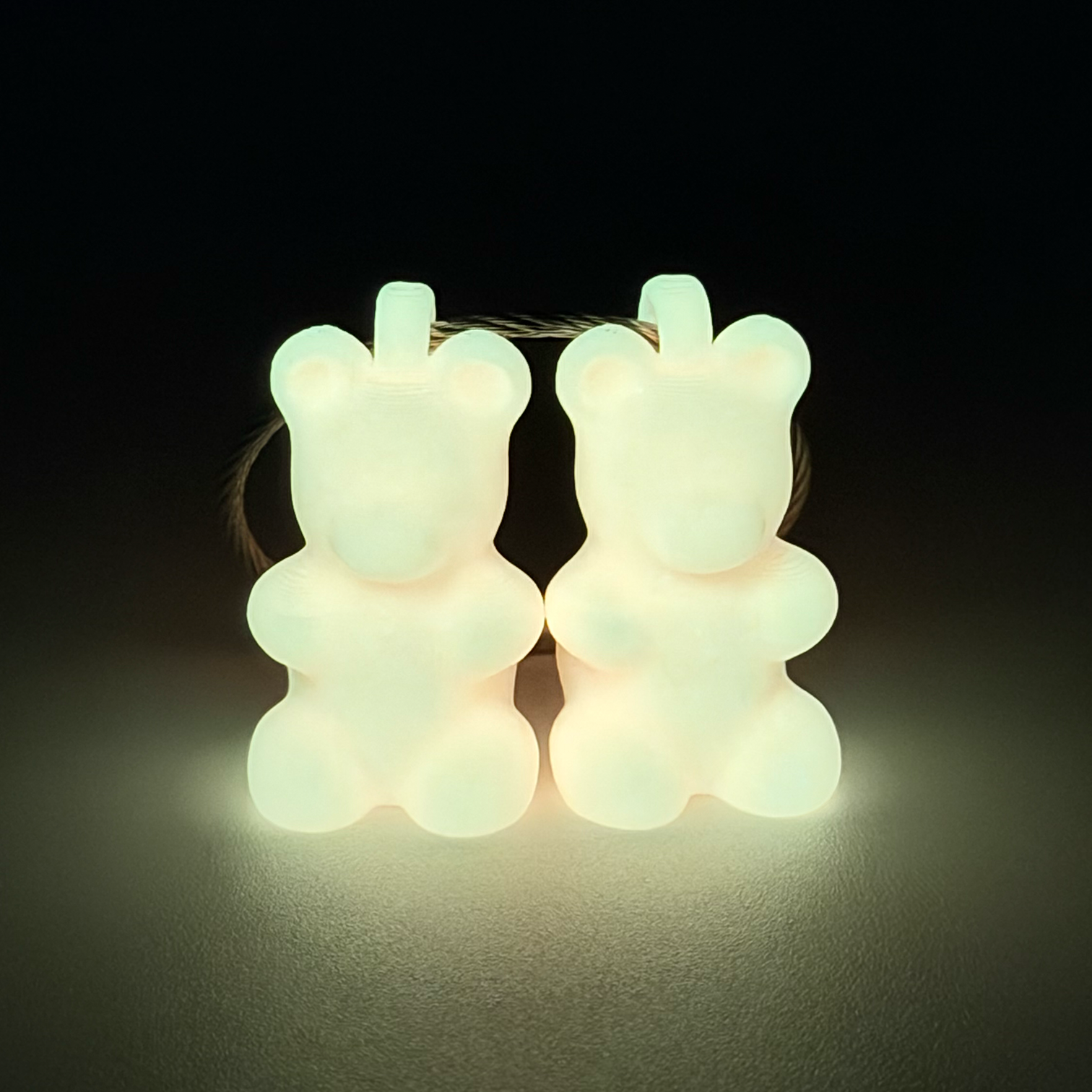 Two orange polylactic acid created using additive manufacturing gummy bear clips on steel cable keyring. Featured attached to a syringe. Shown glowing yellow on a black background.