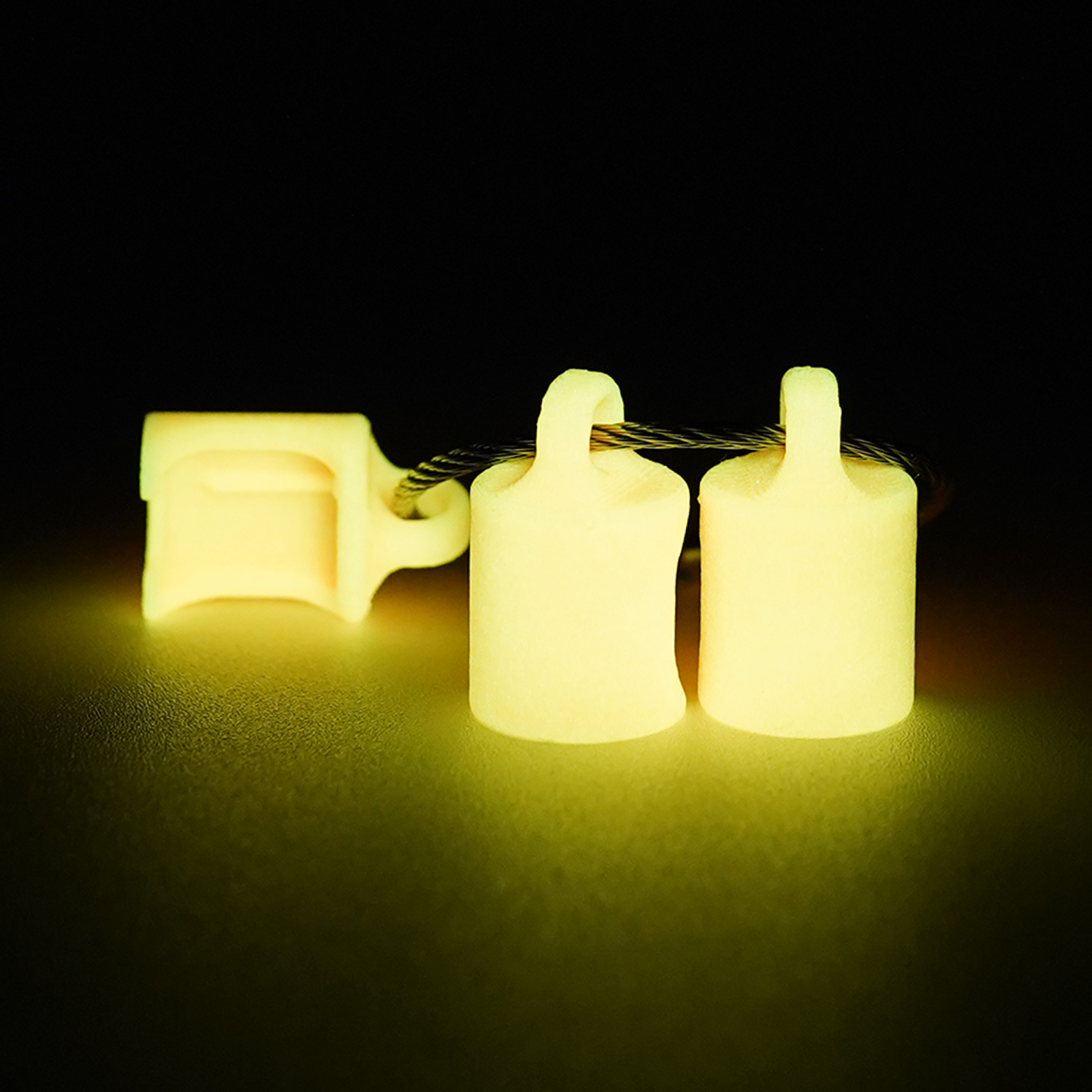 Three orange polylactic acid created using additive manufacturing classic cap clips on steel cable keyring. Shown glowing yellow on a black background.