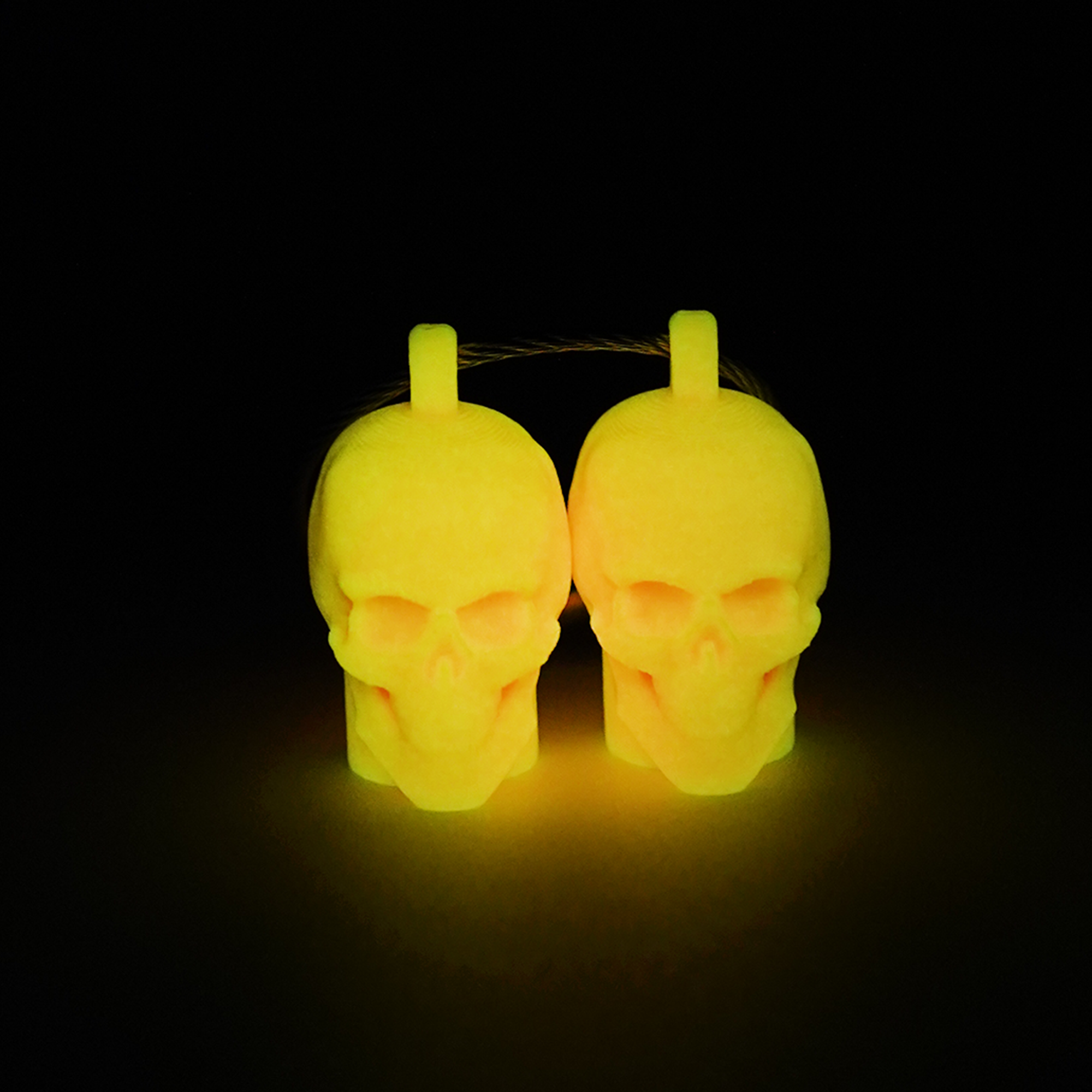 Two orange polylactic acid created using additive manufacturing skull cap clips on steel cable keyring. Shown glowing yellow on a black background.