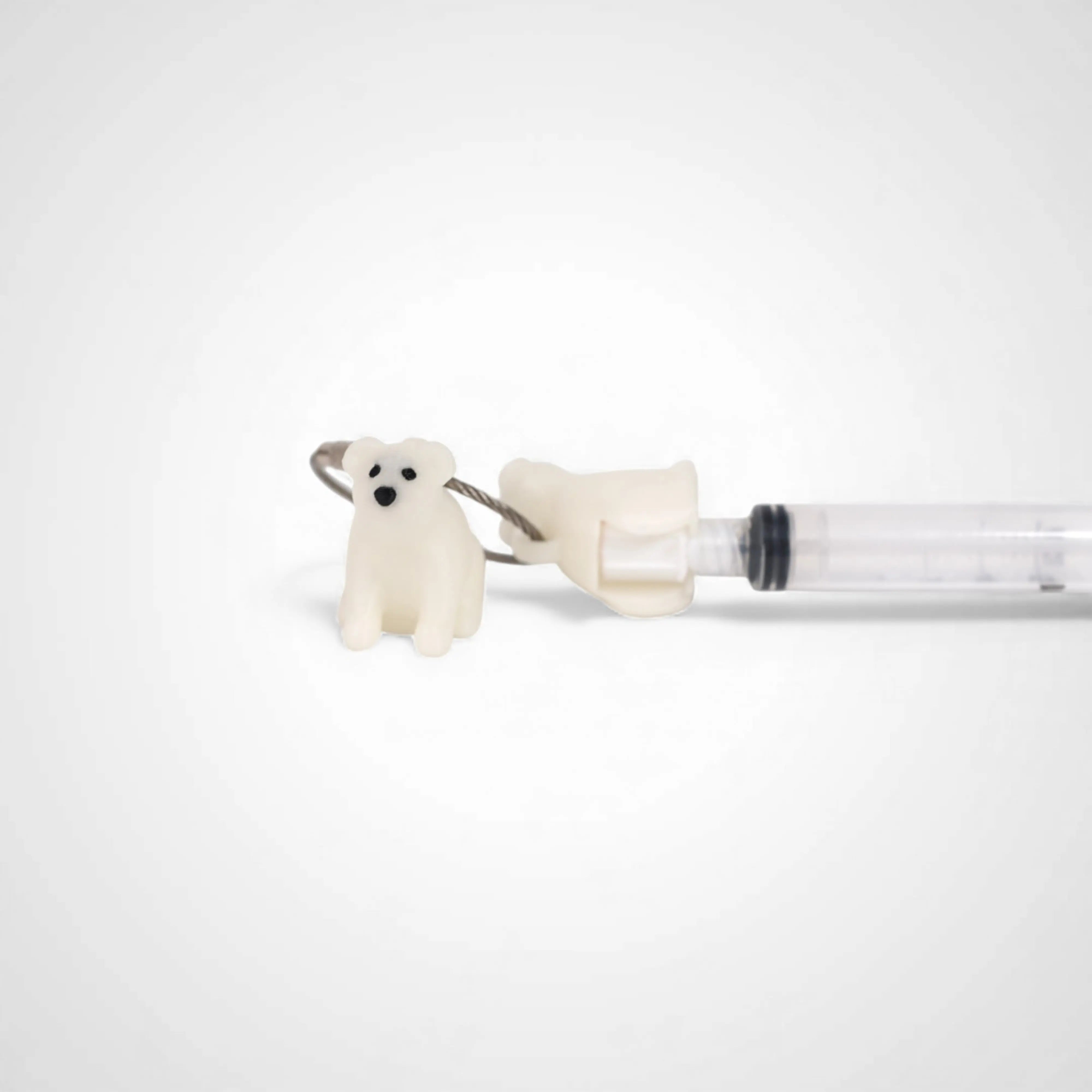 Two white polylactic acid created using additive manufacturing polar bear cap clips on steel cable keyring. Featured attached to a syringe. Shown on a white background.