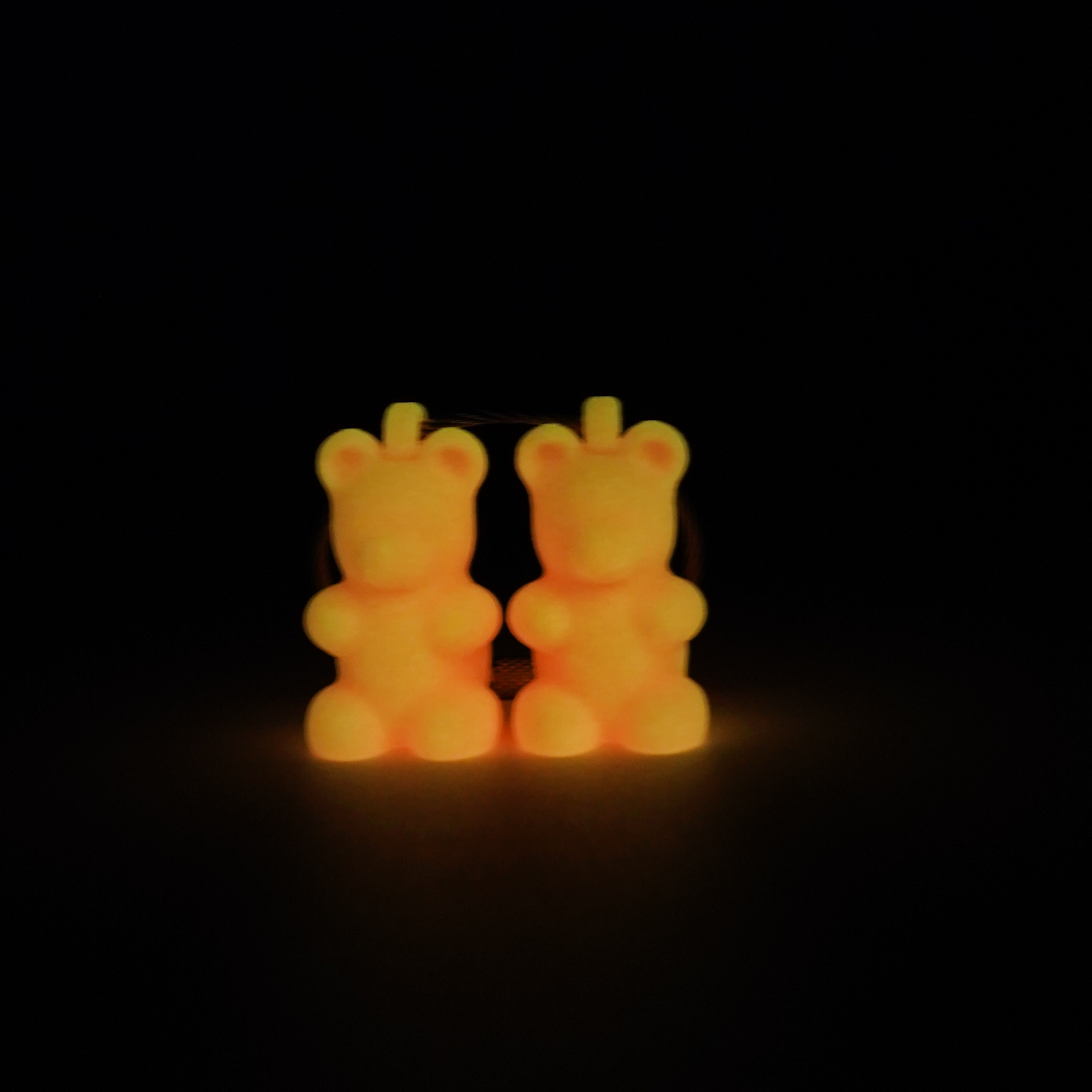 Two pink polylactic acid created using additive manufacturing gummy bear cap clips on steel cable keyring. Shown glowing orange on black background.