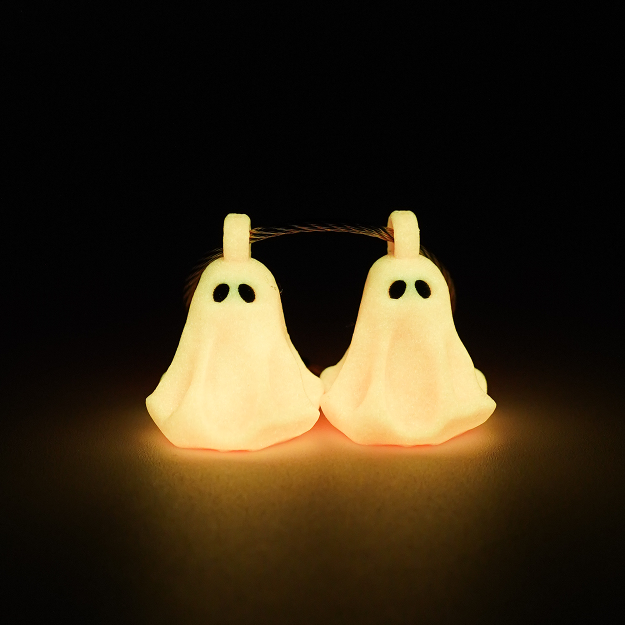 Two pink polylactic acid created using additive manufacturing ghost cap clips on steel cable keyring. Shown glowing orange on a black background.