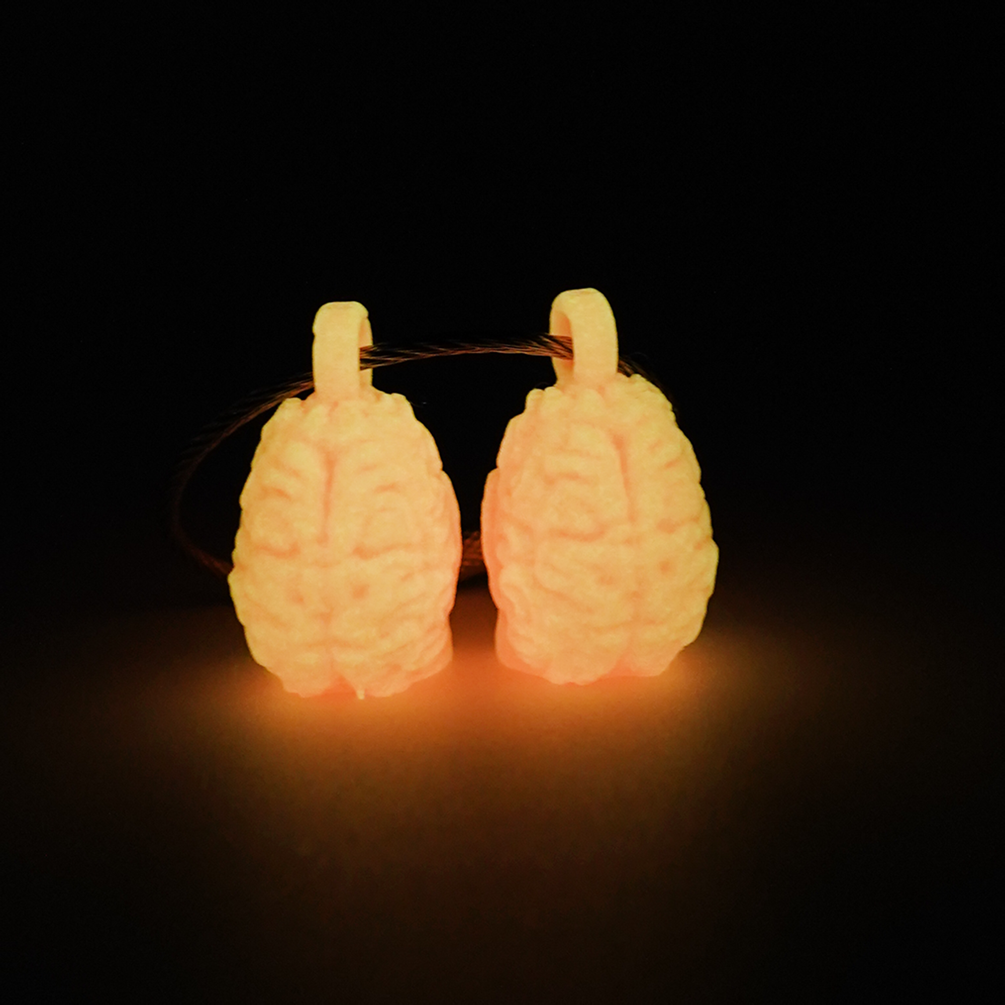 Two pink polylactic acid created using additive manufacturing anatomical brain cap clips on steel cable keyring. Shown glowing orange on a black background.