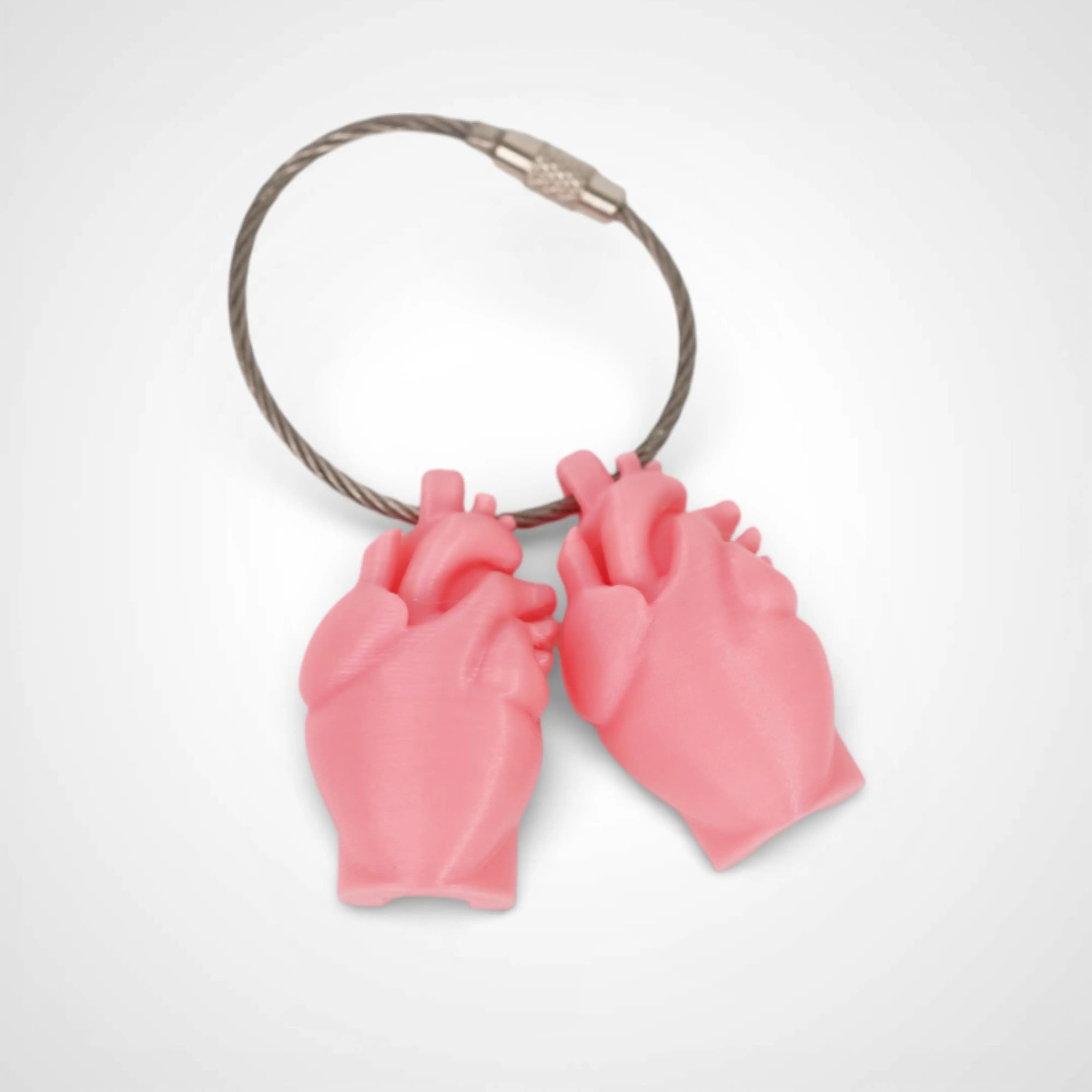 Two pink polylactic acid created using additive manufacturing anatomical heart cap clips on steel cable keyring. Shown on a white background.