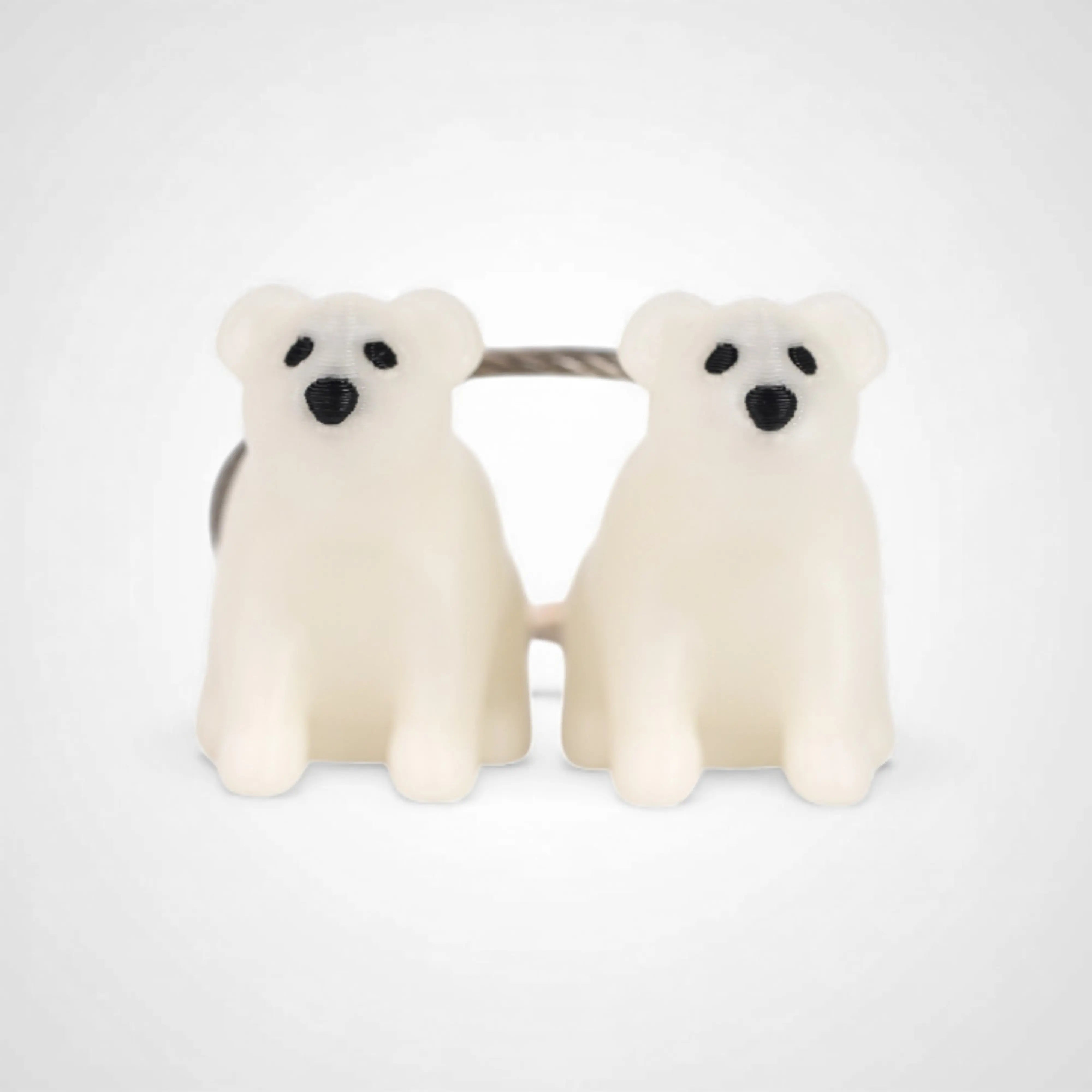 Two white polylactic acid created using additive manufacturing polar bear cap clips on steel cable keyring. Shown on a white background.