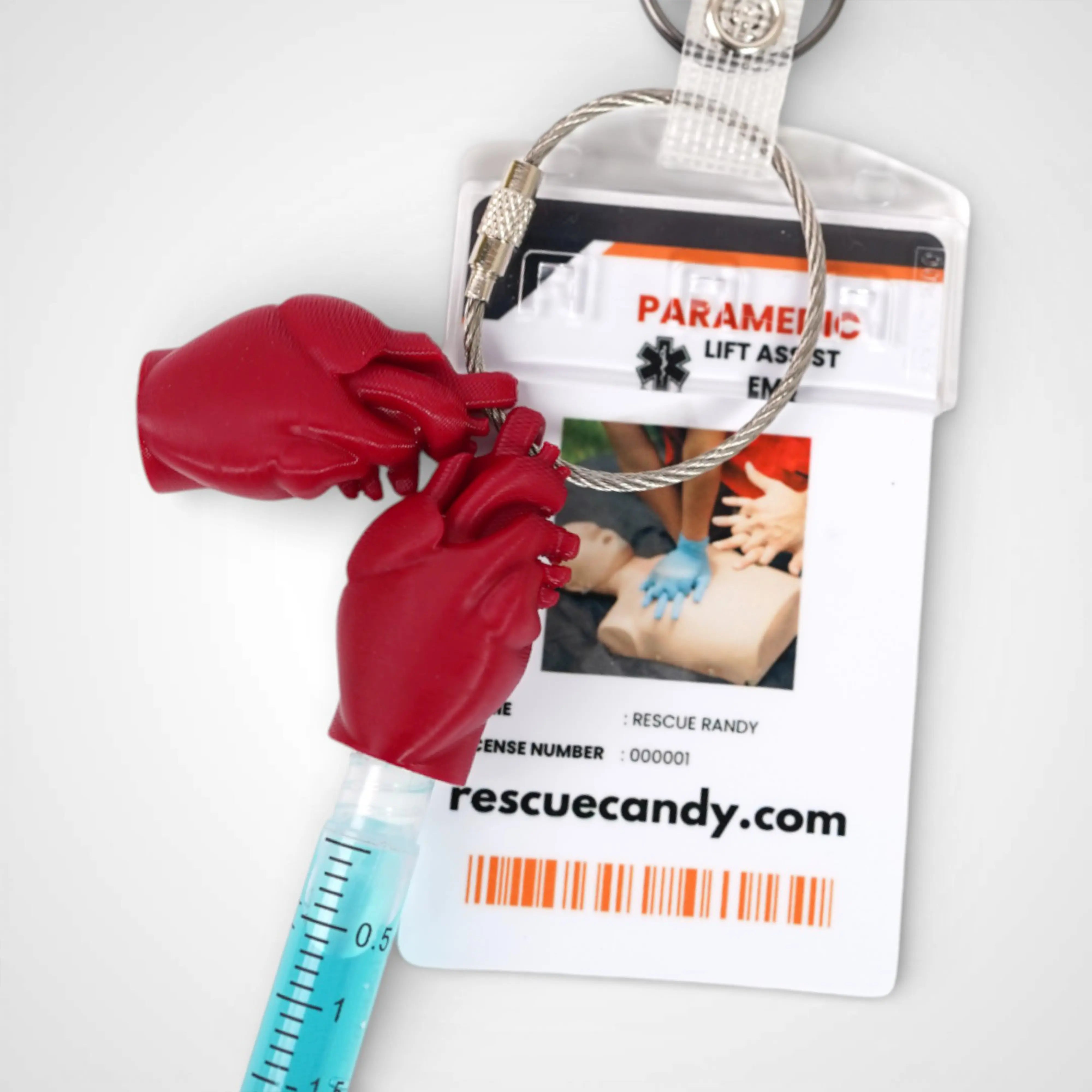 Two red polylactic acid created using additive manufacturing anatomical heart cap clips on steel cable keyring. Featured attached to a badge. Shown on a white background.