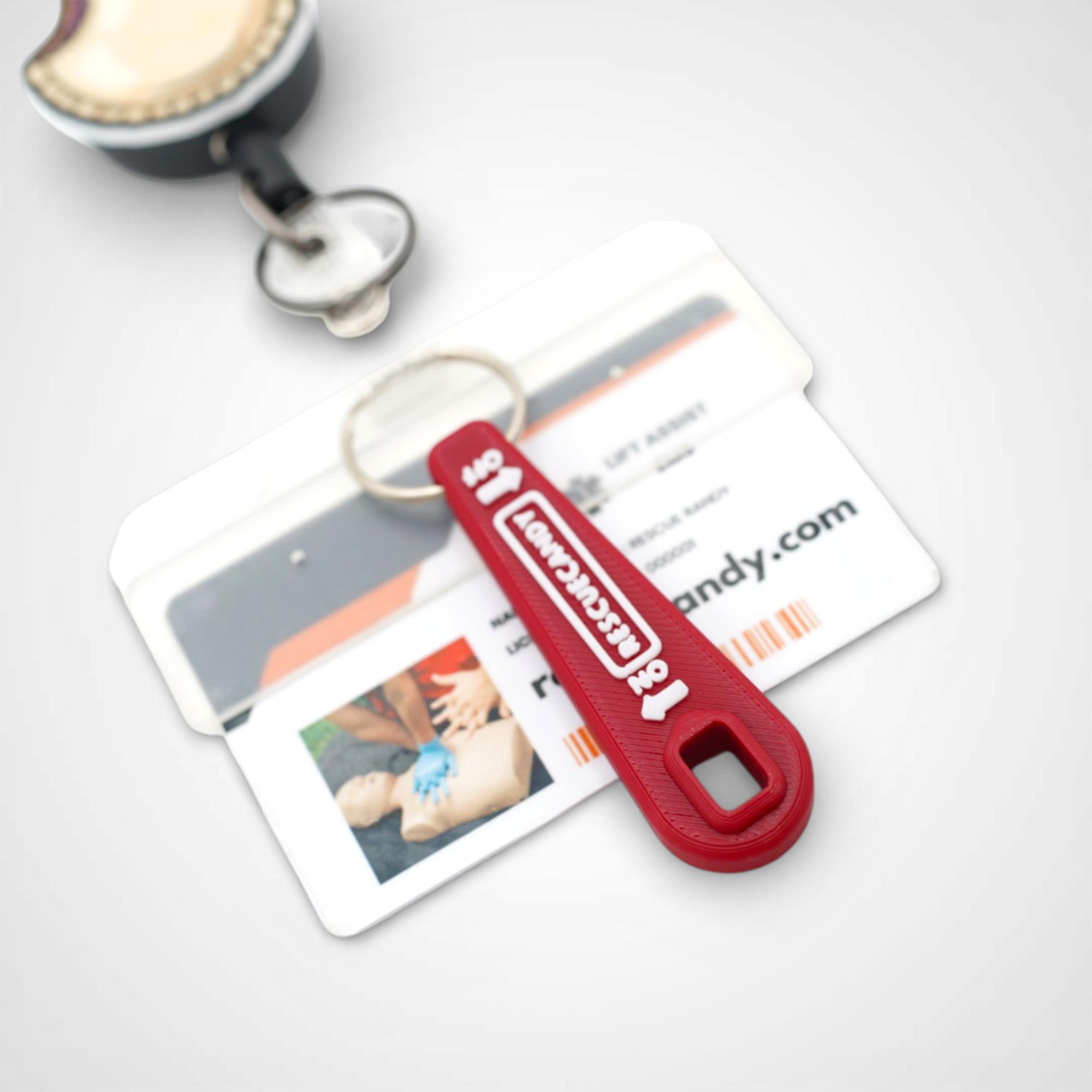 Mini red Oxygen Wrench. Made to fit CGA-870 valves. Shown attached to badge on white background.