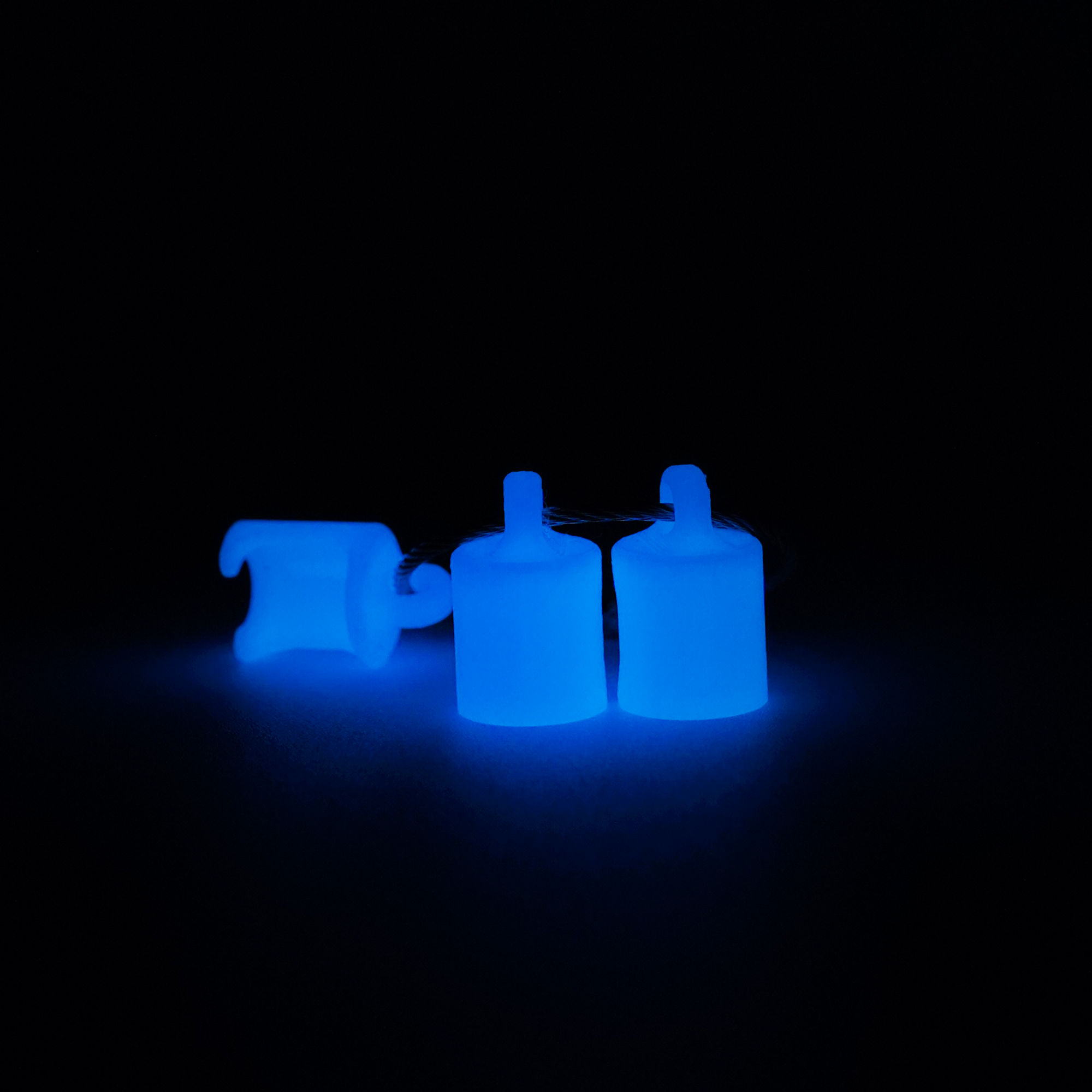 Three white polylactic acid created using additive manufacturing classic cap clips on steel cable keyring. Shown glowing blue on black background.