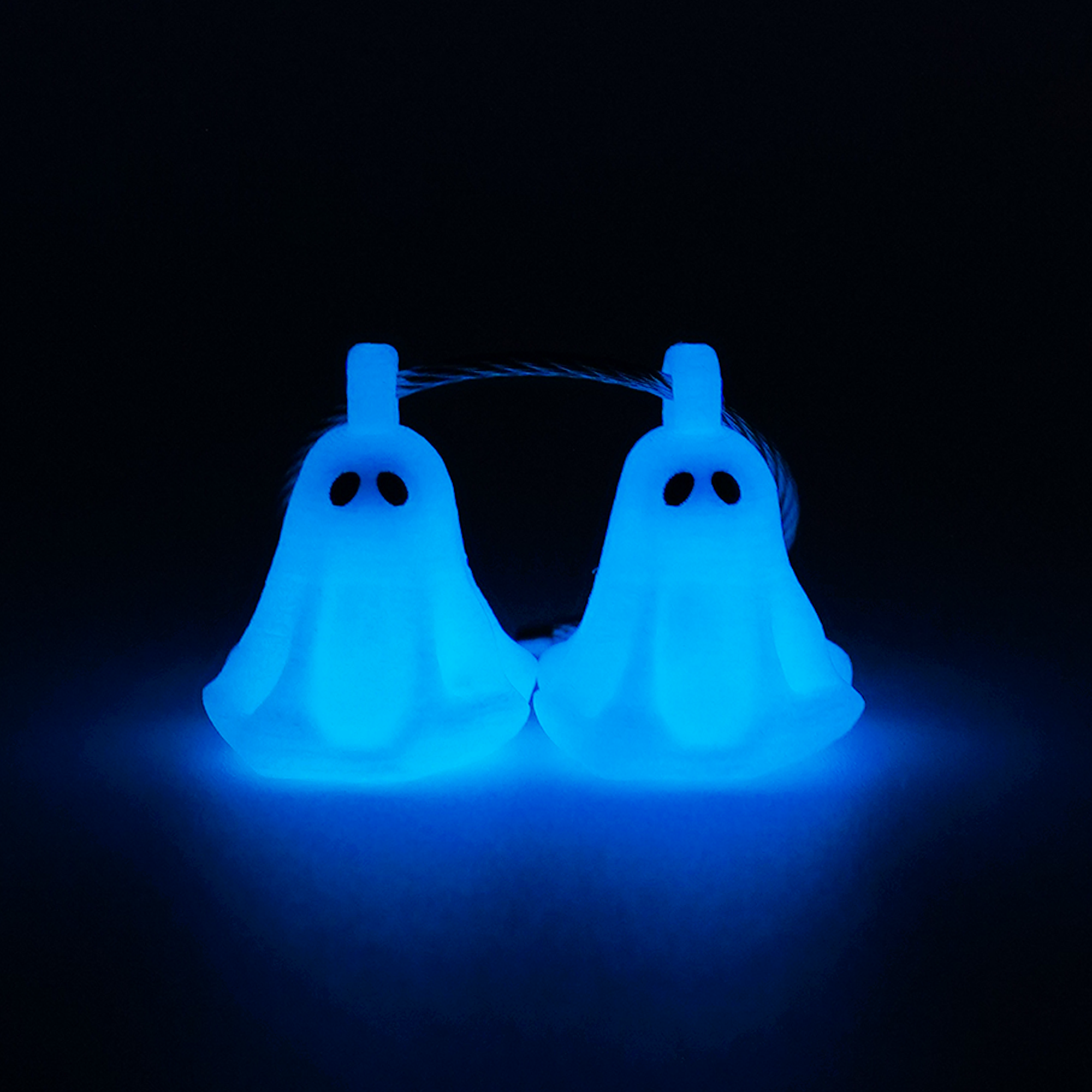 Two white polylactic acid created using additive manufacturing ghost cap clips on steel cable keyring. Shown glowing blue on a black background.
